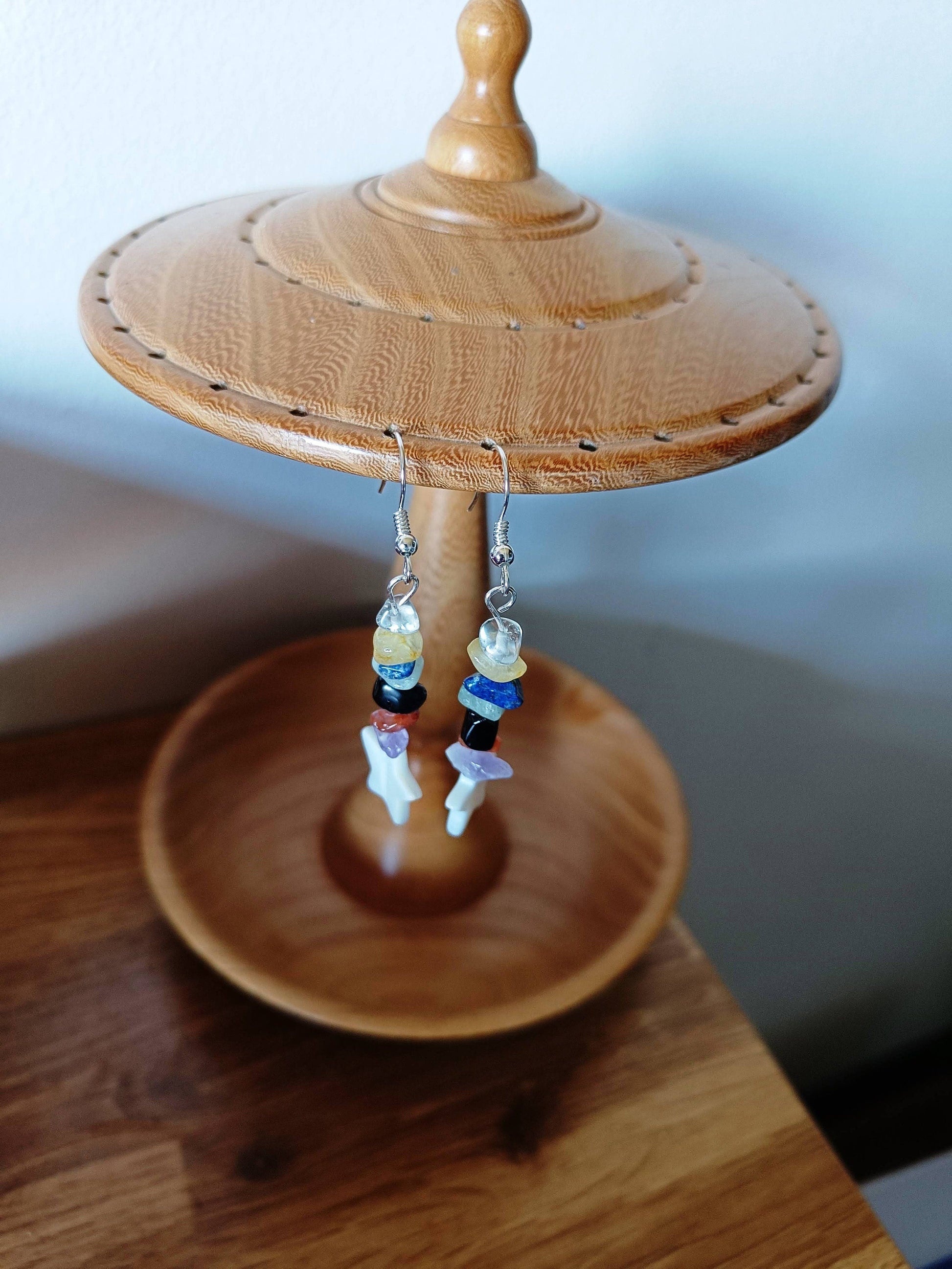 Multicoloured star earrings with repurposed glass, gemstone chips, and white star-shaped shell on a wooden stand.