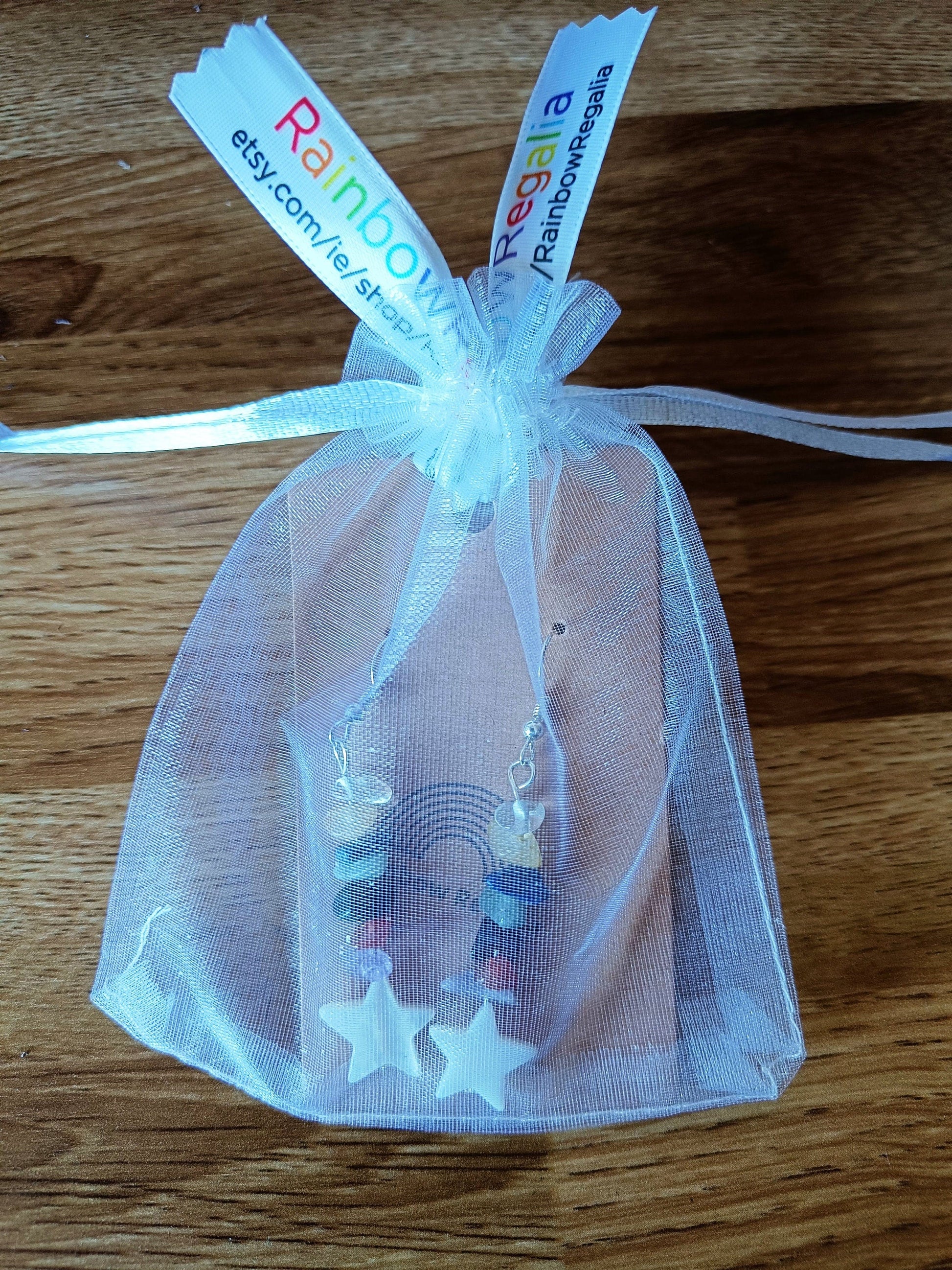 Multicoloured star earrings with gemstone chips and white star shell in a gift bag.