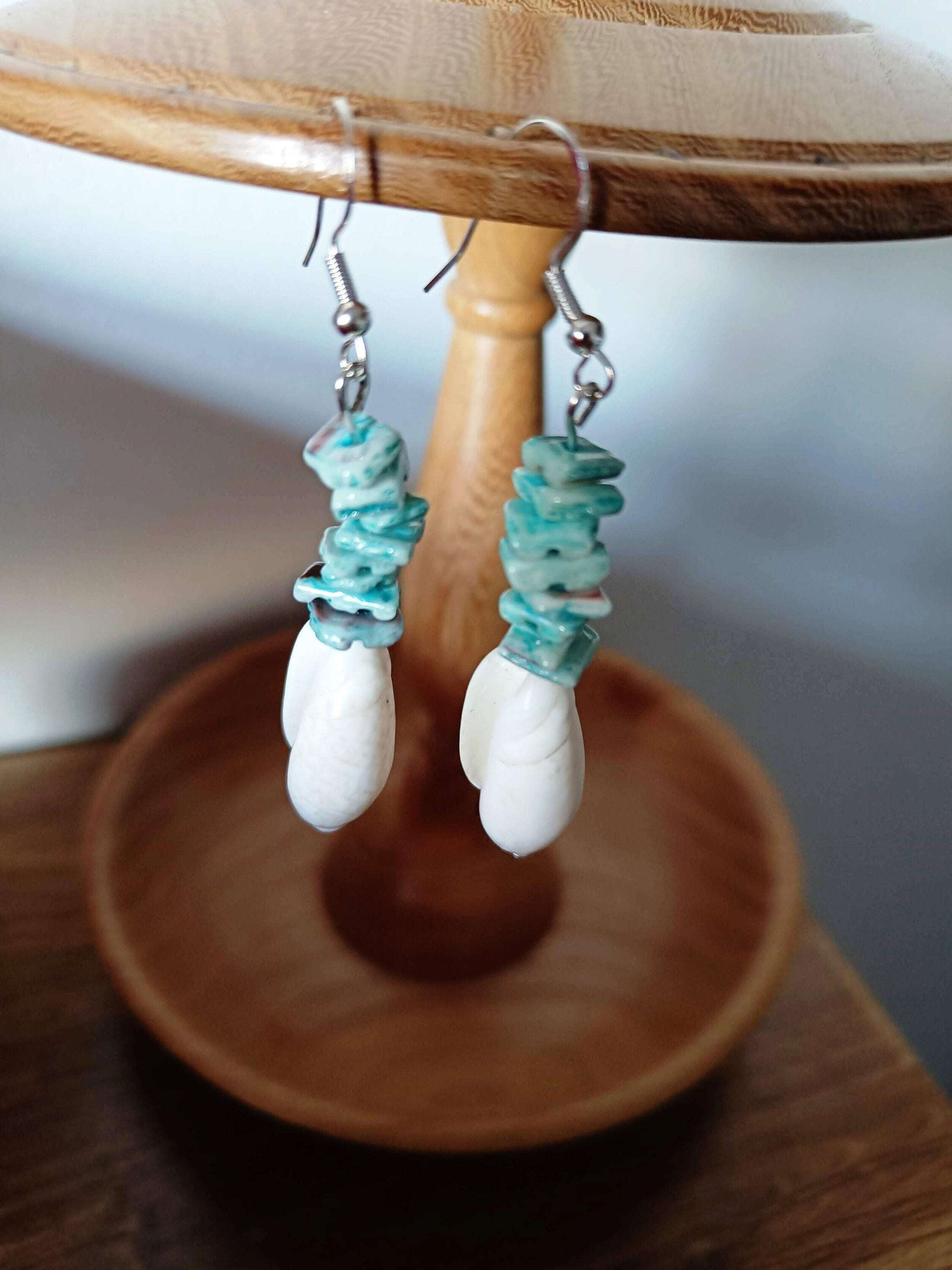 Turquoise and white shell dangle earrings on wooden display.