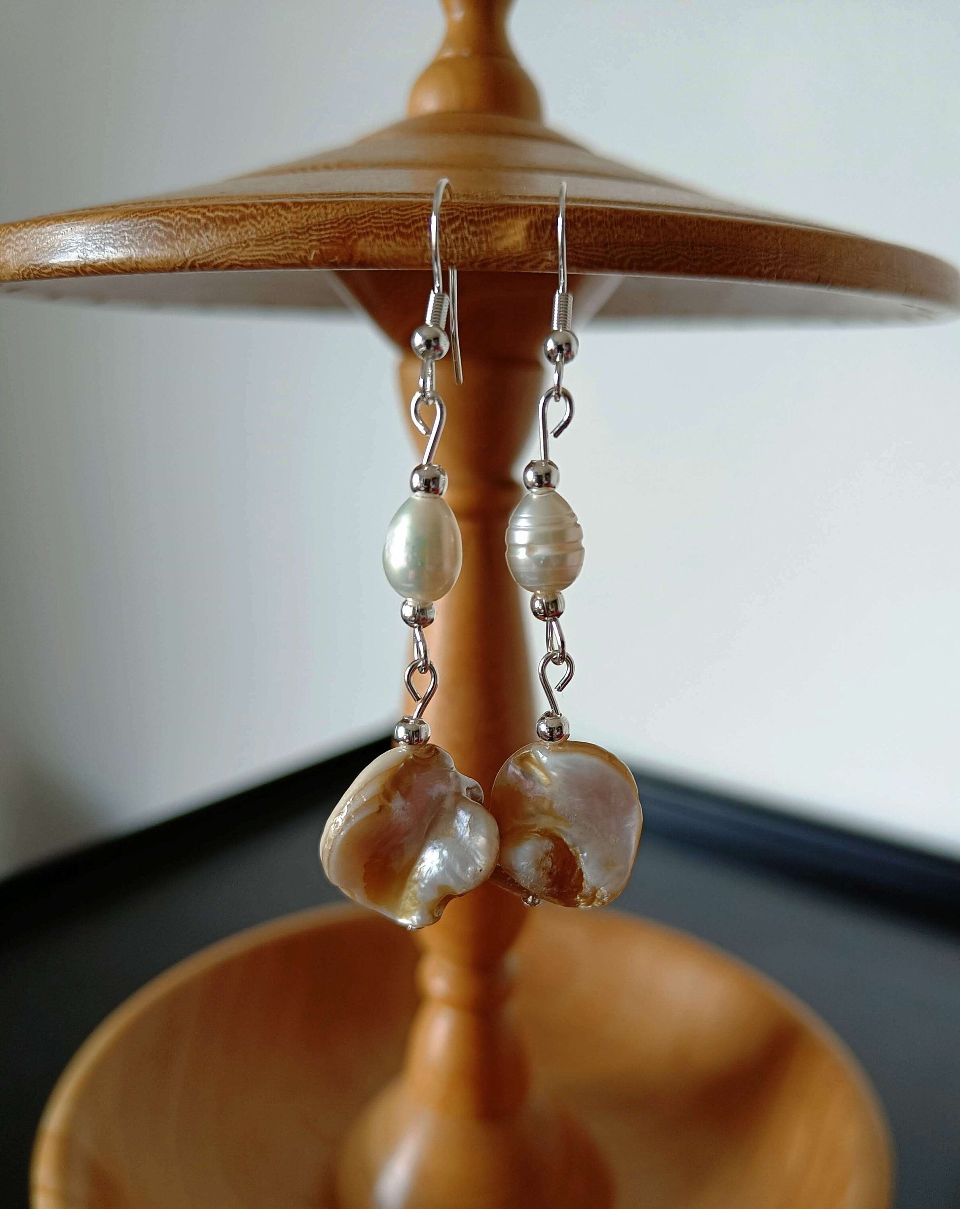 Long freshwater pearl earrings with mother of pearl dangles and silver-plated beads on a wooden stand.