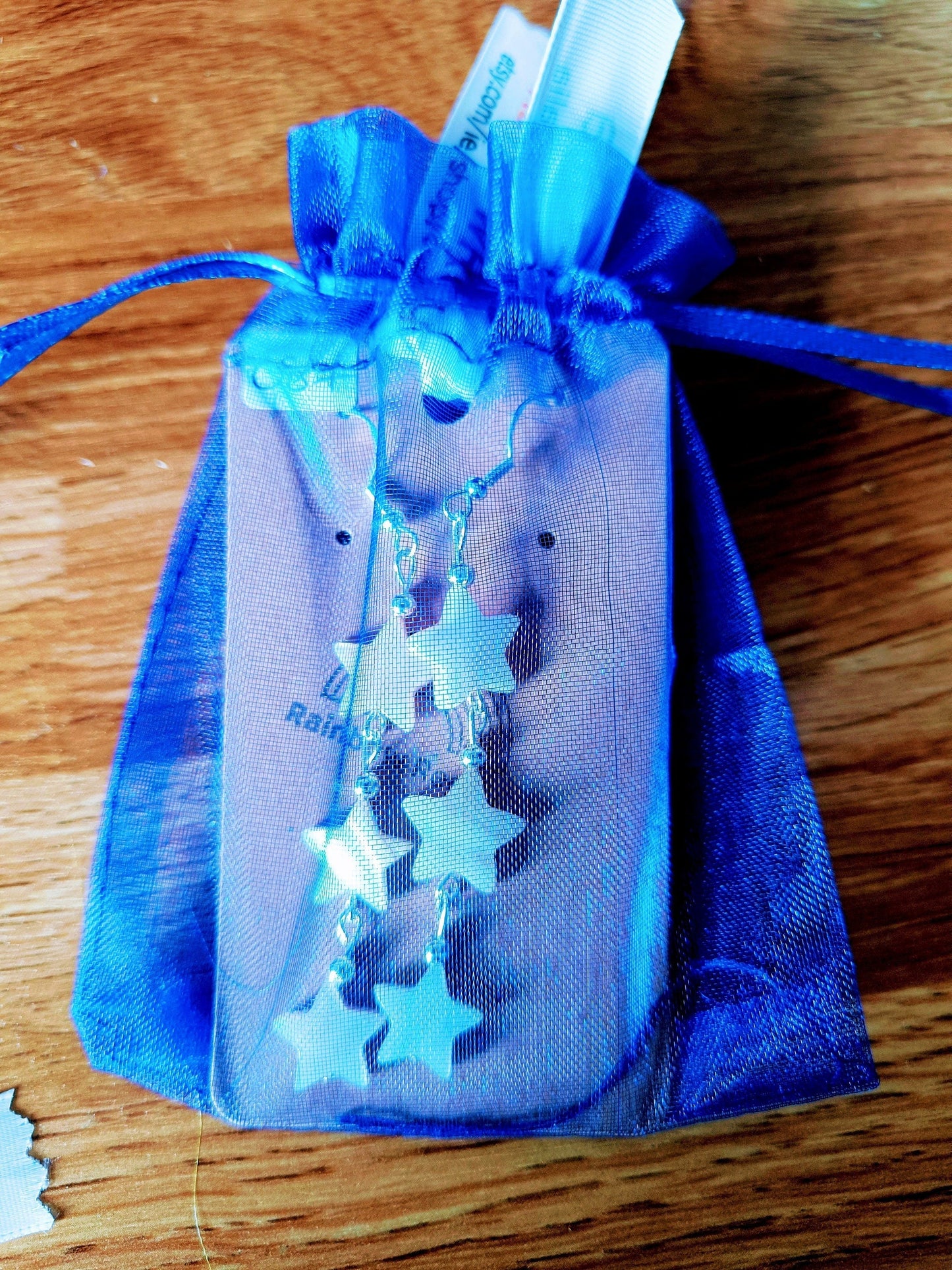 Maurea Mother of Pearl Star Silver Earrings in blue organza bag, featuring delicate mother of pearl star dangles, on a wooden surface.