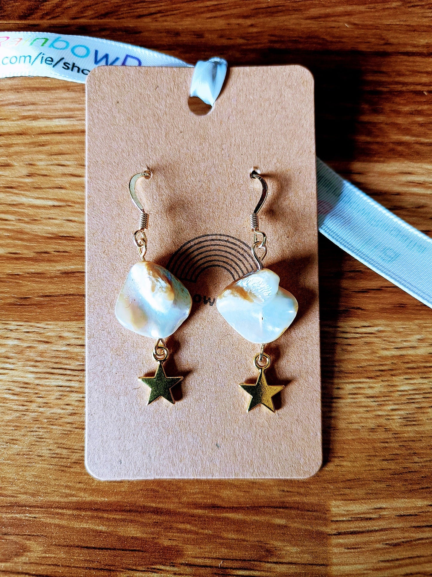 Celeste Gold Star freshwater pearl earrings with gold star charms on wooden background.