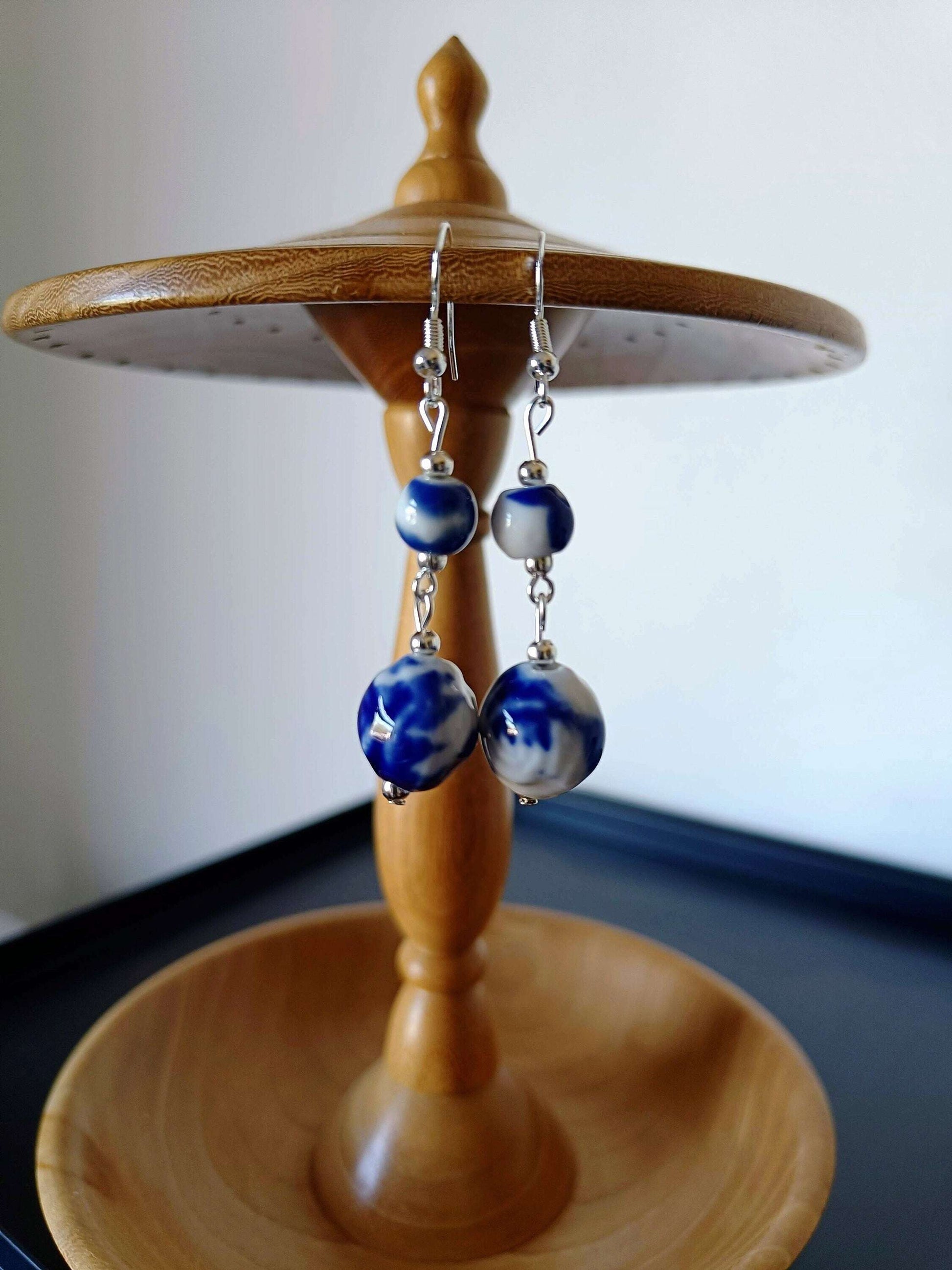 Blue and white ceramic earrings with Delft pottery-inspired beads on a wooden stand.