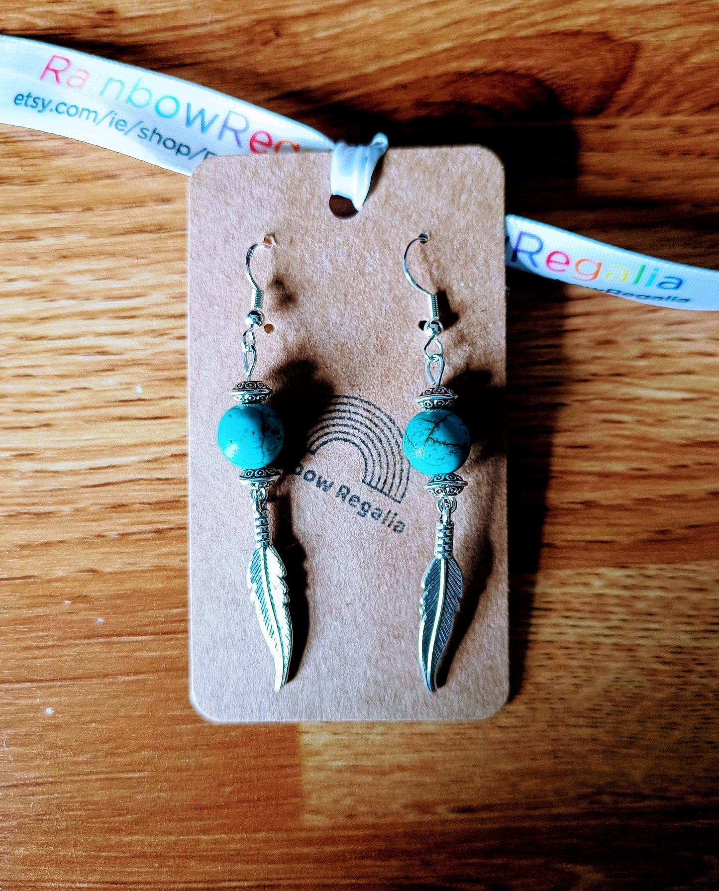 Tallulah Feather Earrings with turquoise beads and antique silver plated feathers on a wooden background.