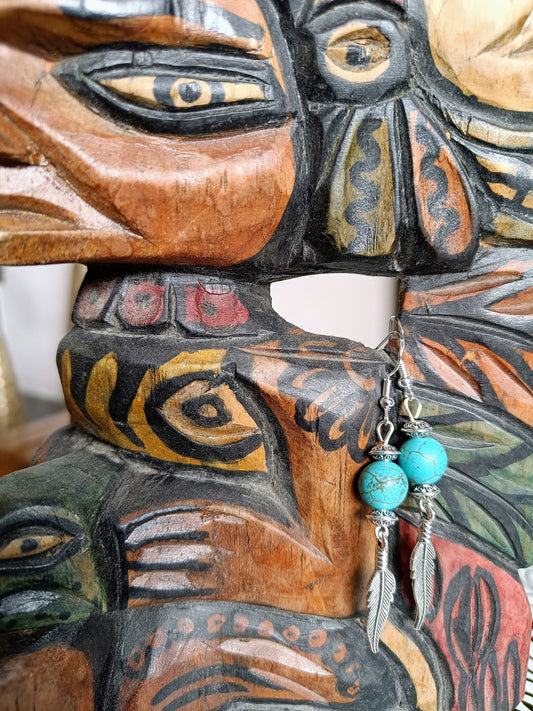 Tallulah Feather Earrings with turquoise beads and silver plated feathers on a carved wooden mask backdrop.