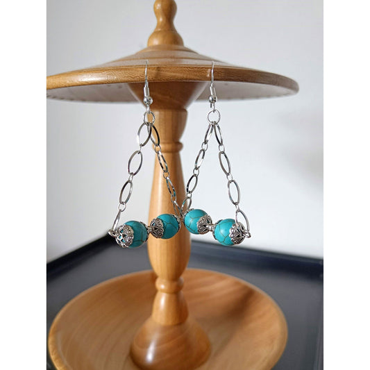 Silver and turquoise chandelier earrings with repurposed turquoise beads and stainless steel chain displayed on a wooden stand.