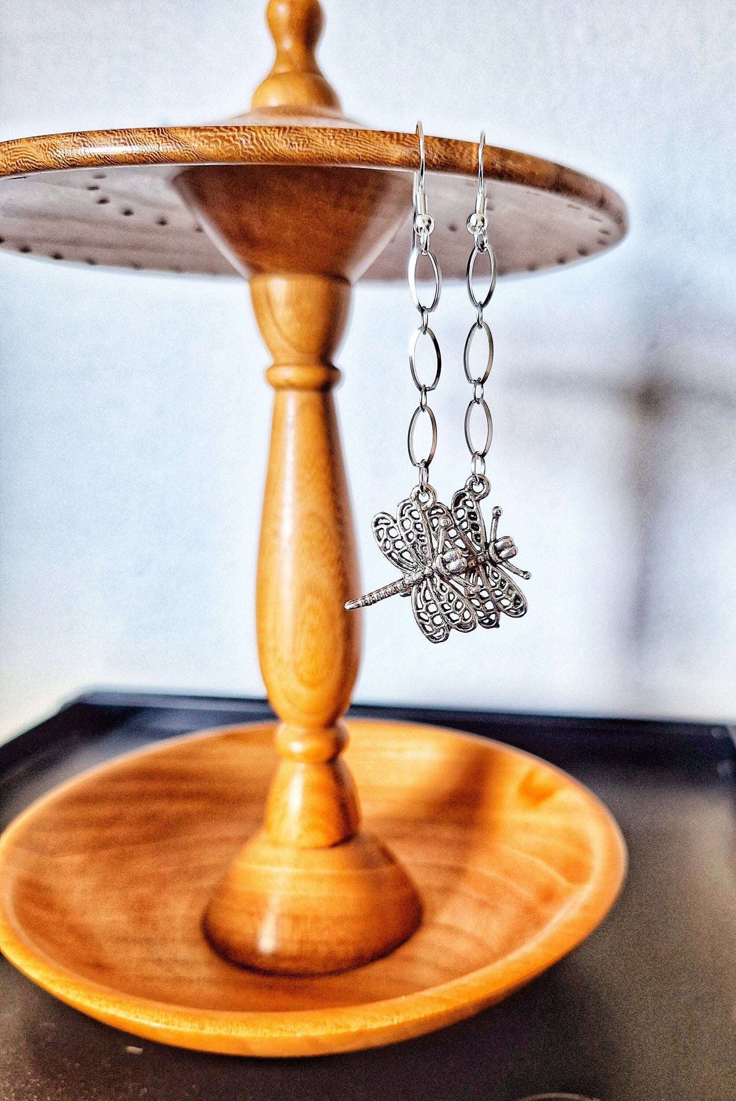 Long silver dragonfly dangle earrings on wooden stand.