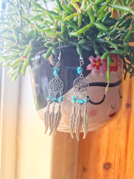 Turquoise Dream Catcher Earrings with feather charms and genuine turquoise chips hanging on a potted plant.