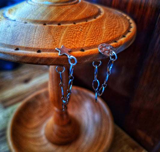 Siouxsie Chain Drop Earrings with stainless steel chain and star or disc studs on wooden display.