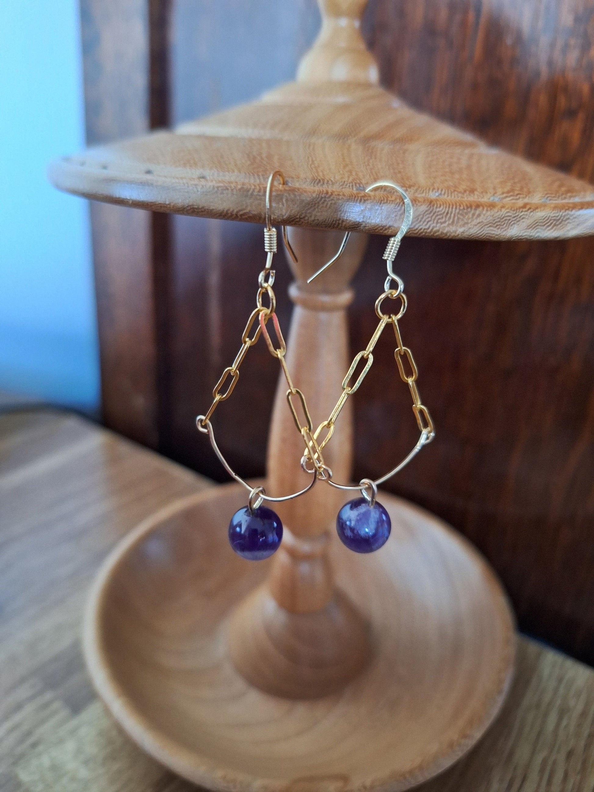 Heather Chandelier Earrings with amethyst beads on a wooden stand.