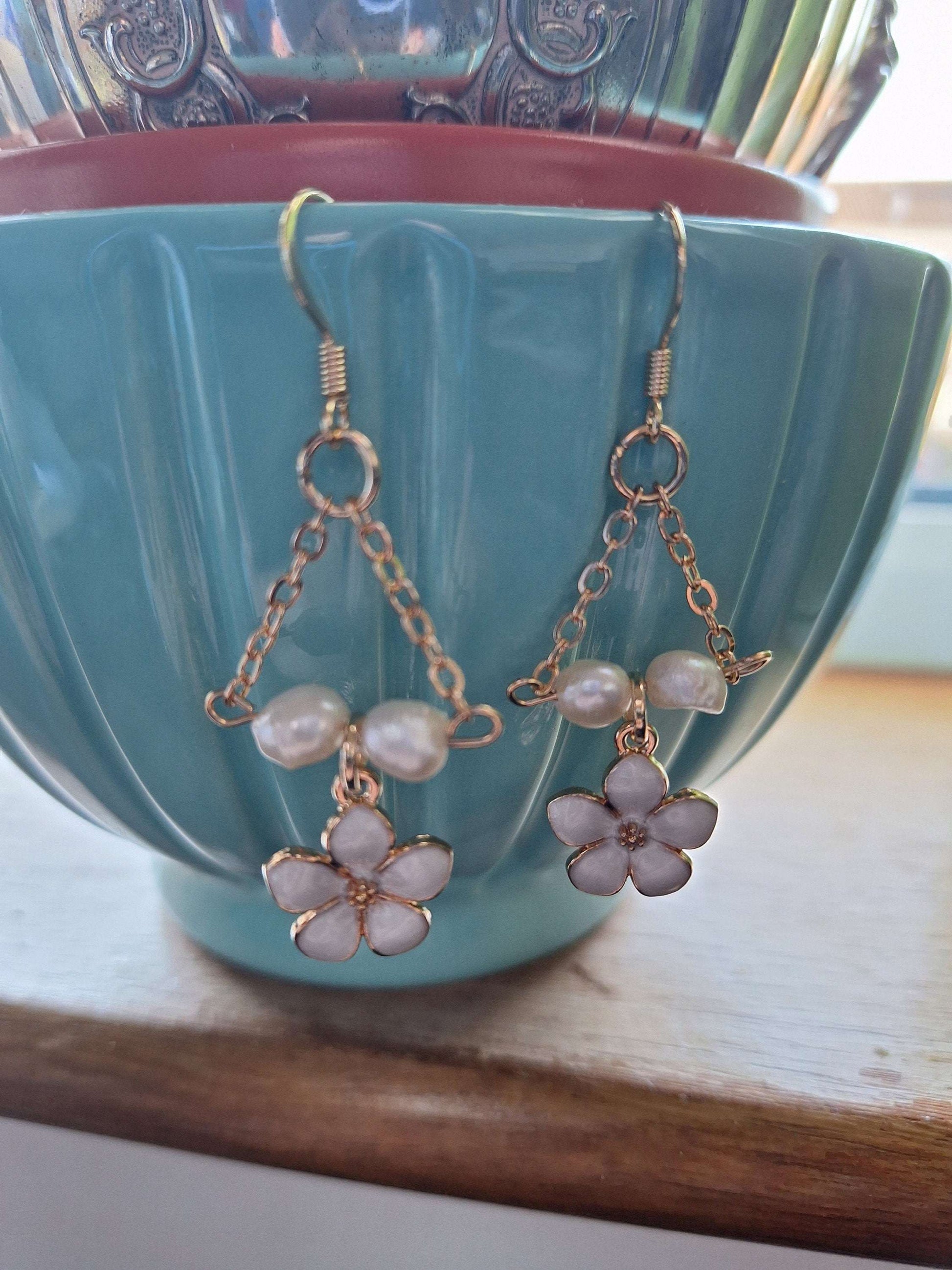 Naomi Cherry Blossom Pearl Earrings with gold-plated chain and freshwater pearls displayed on a turquoise ceramic cup.