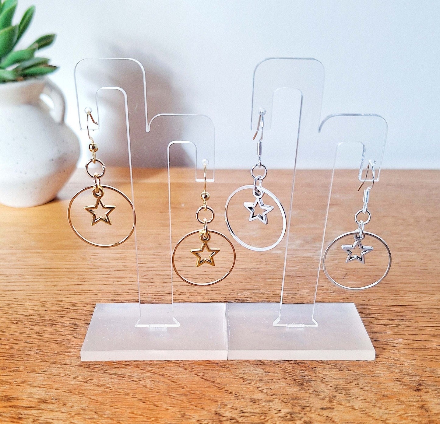 Vega Star Earrings in silver and gold with celestial design on clear stands.