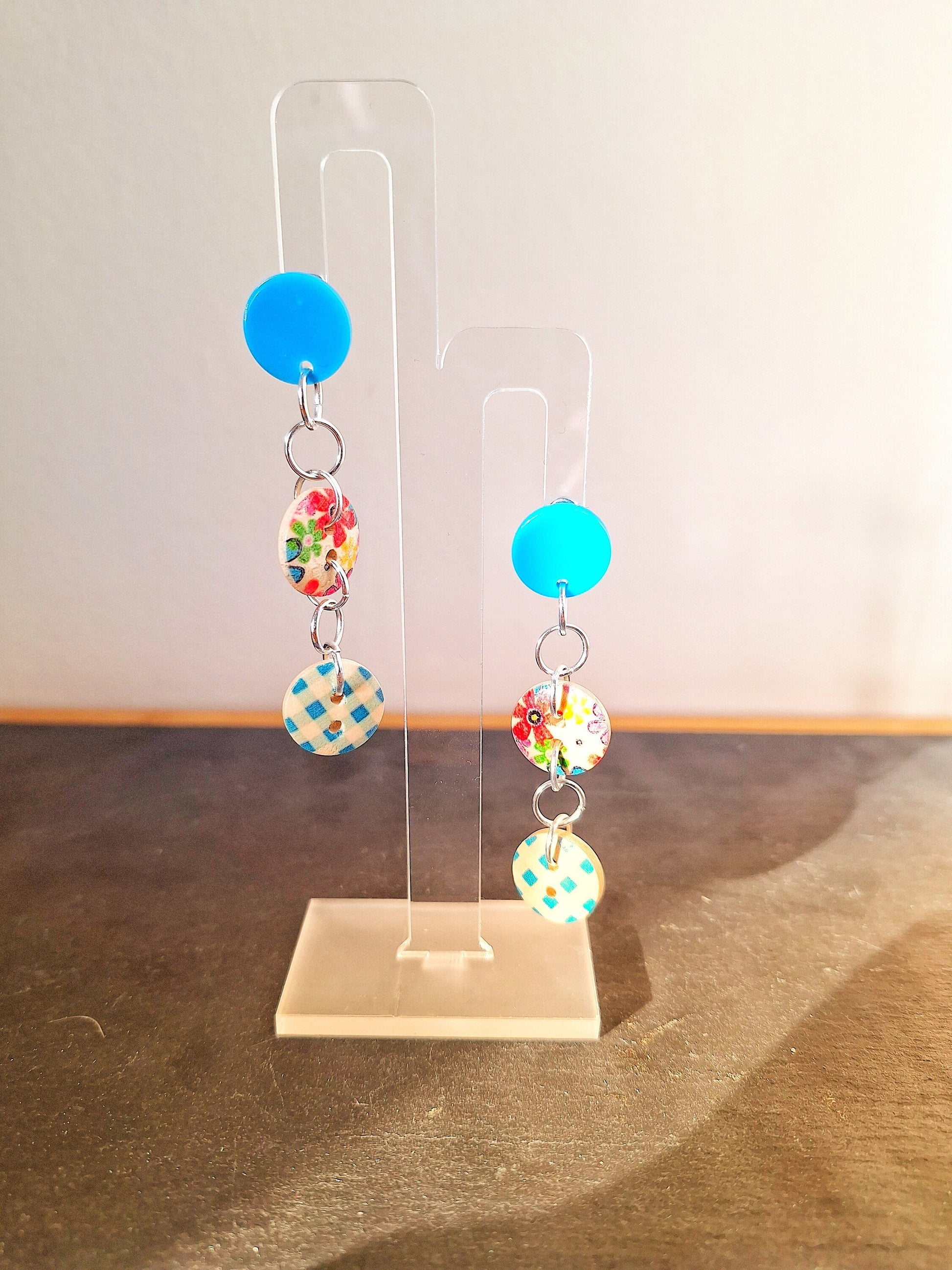Bella Button Earrings in blue and pink with wooden buttons and acrylic discs on display stand.