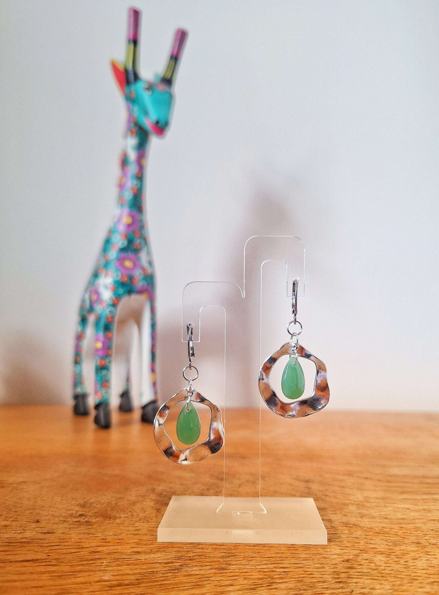 Jade green earrings with teardrop beads on stainless steel huggie hoops displayed on a stand.