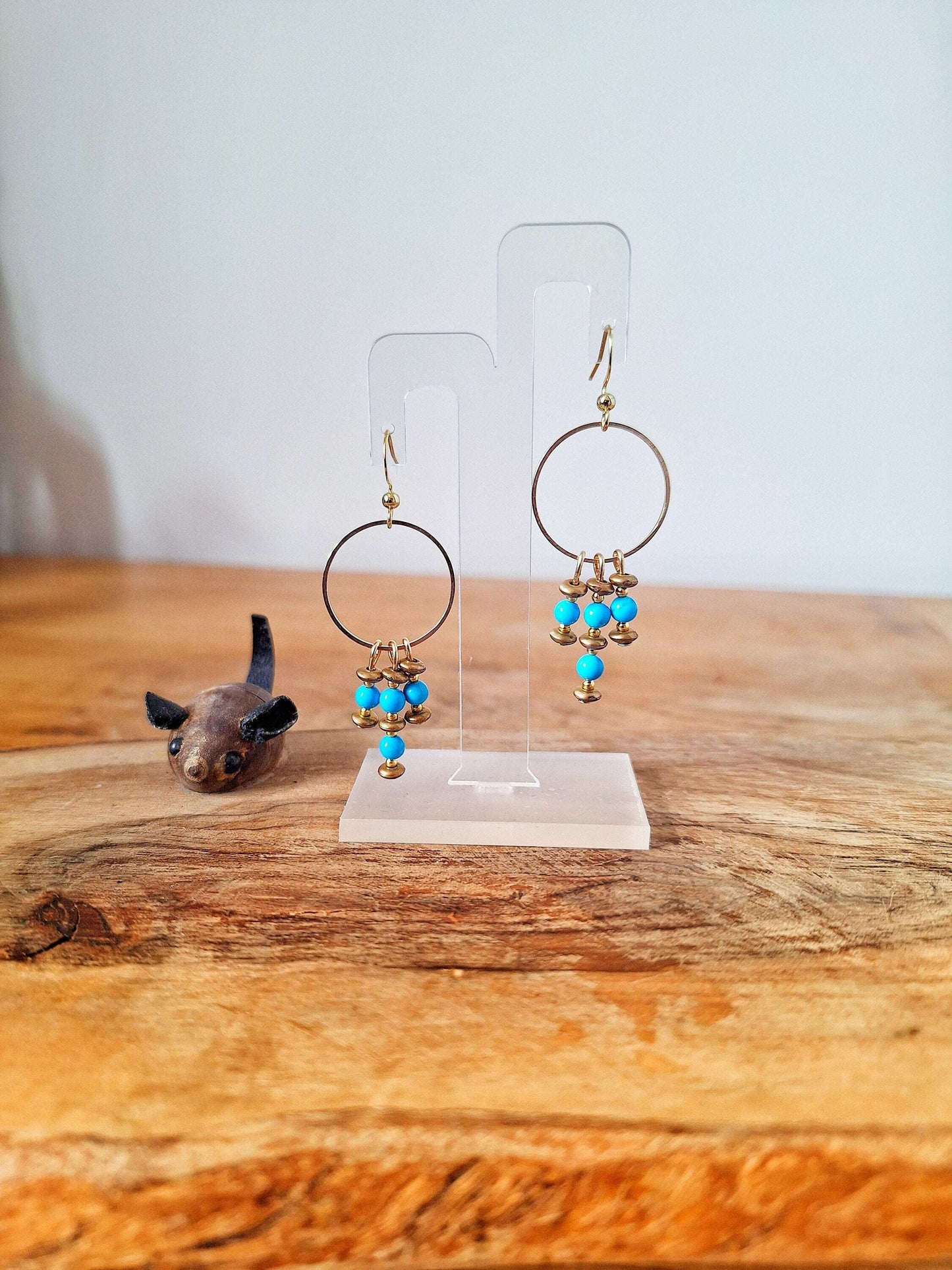 Suzanne Turquoise Chandelier Earrings with turquoise stone beads, bronze details, and gold-plated accents on a wooden display.
