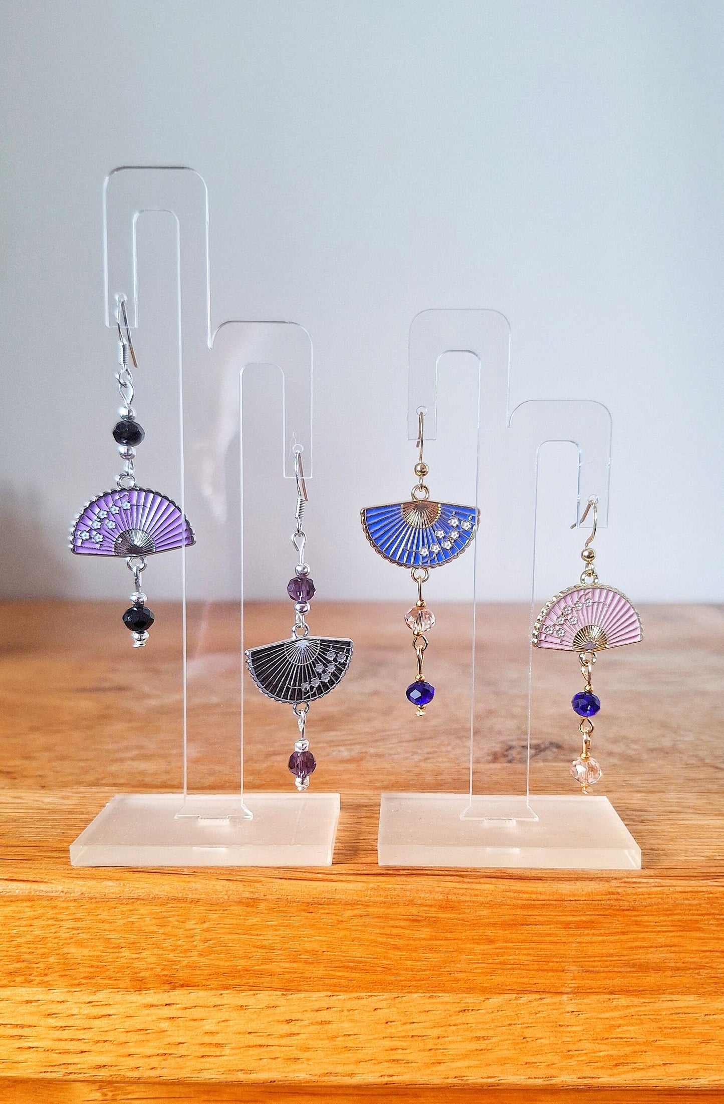 Fumika Fan Earrings with faceted glass beads, fan charms, and gold-plated or sterling silver findings displayed on stands.