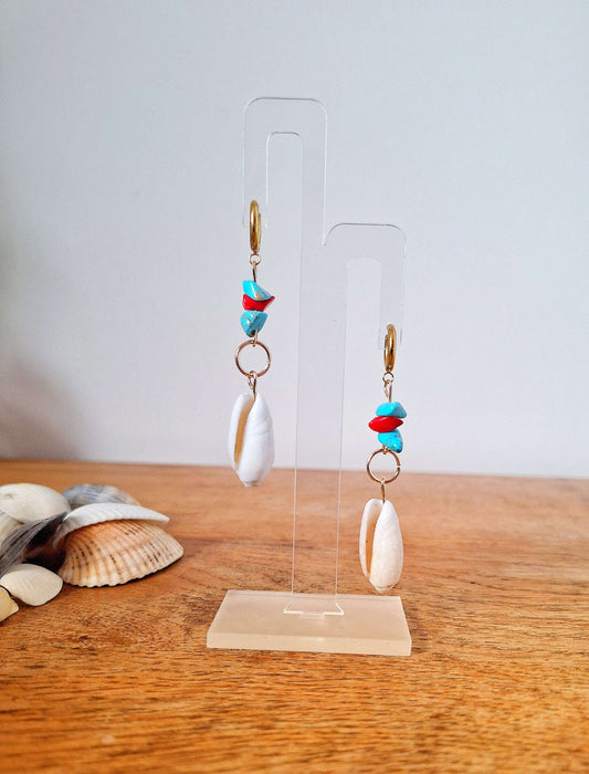 Ariel turquoise and coral shell earrings on display stand with conch shells nearby.