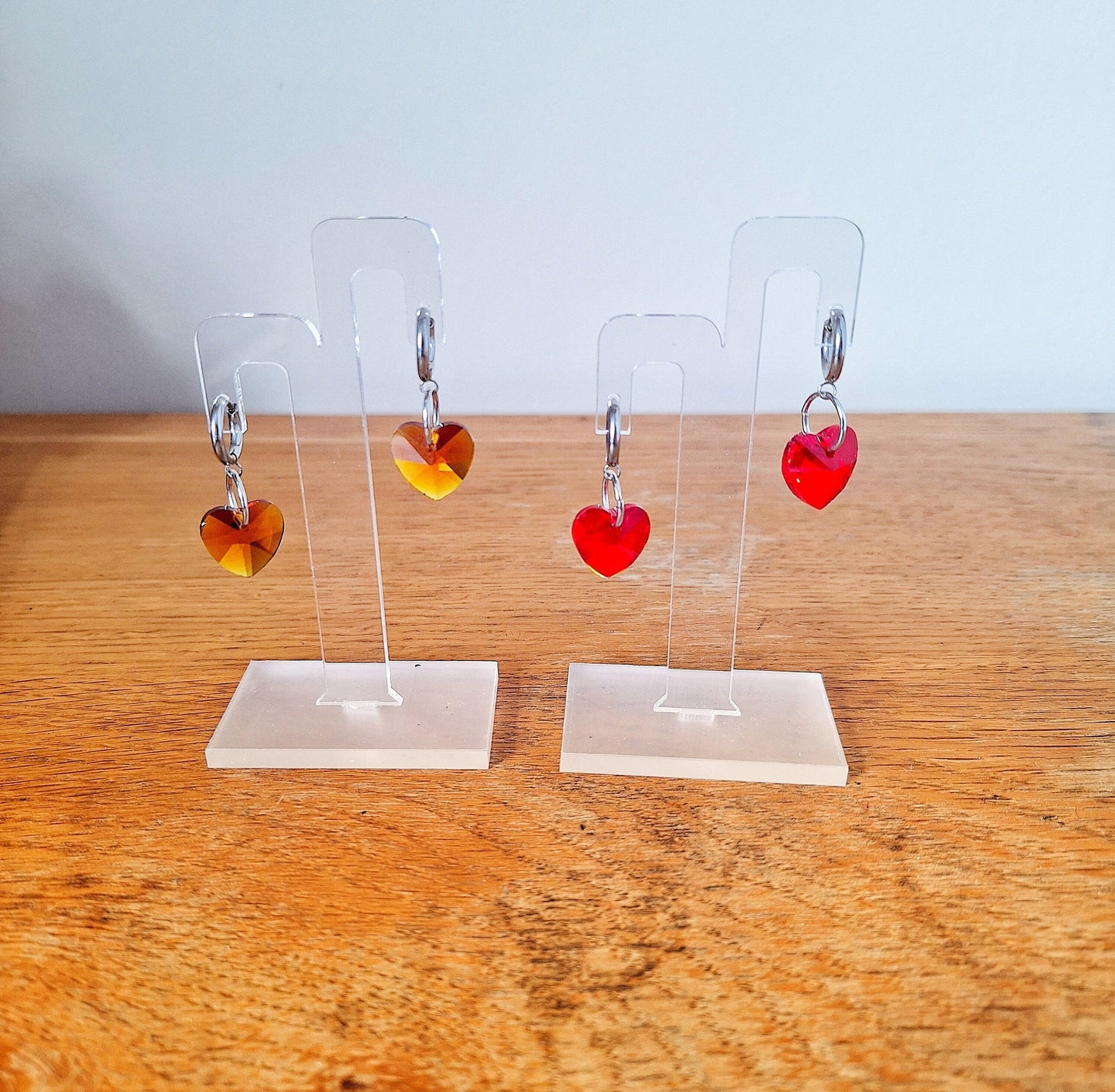 Venus Crystal Heart Huggies with faceted glass heart beads on stainless steel hoops, displayed in various colors.