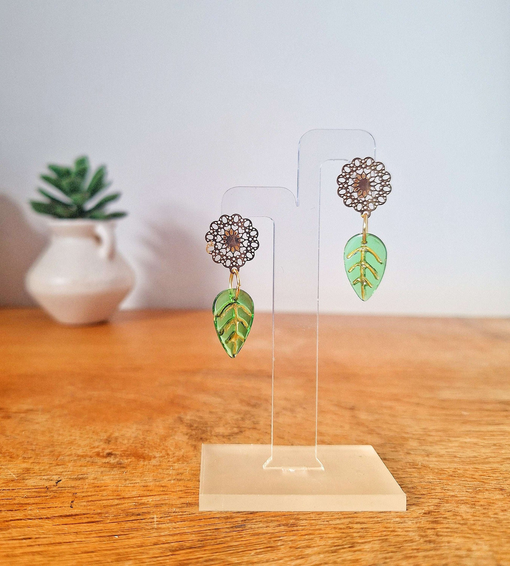 Gold Leaf Earrings with green glass leaves on gold-plated studs displayed on a wooden surface.