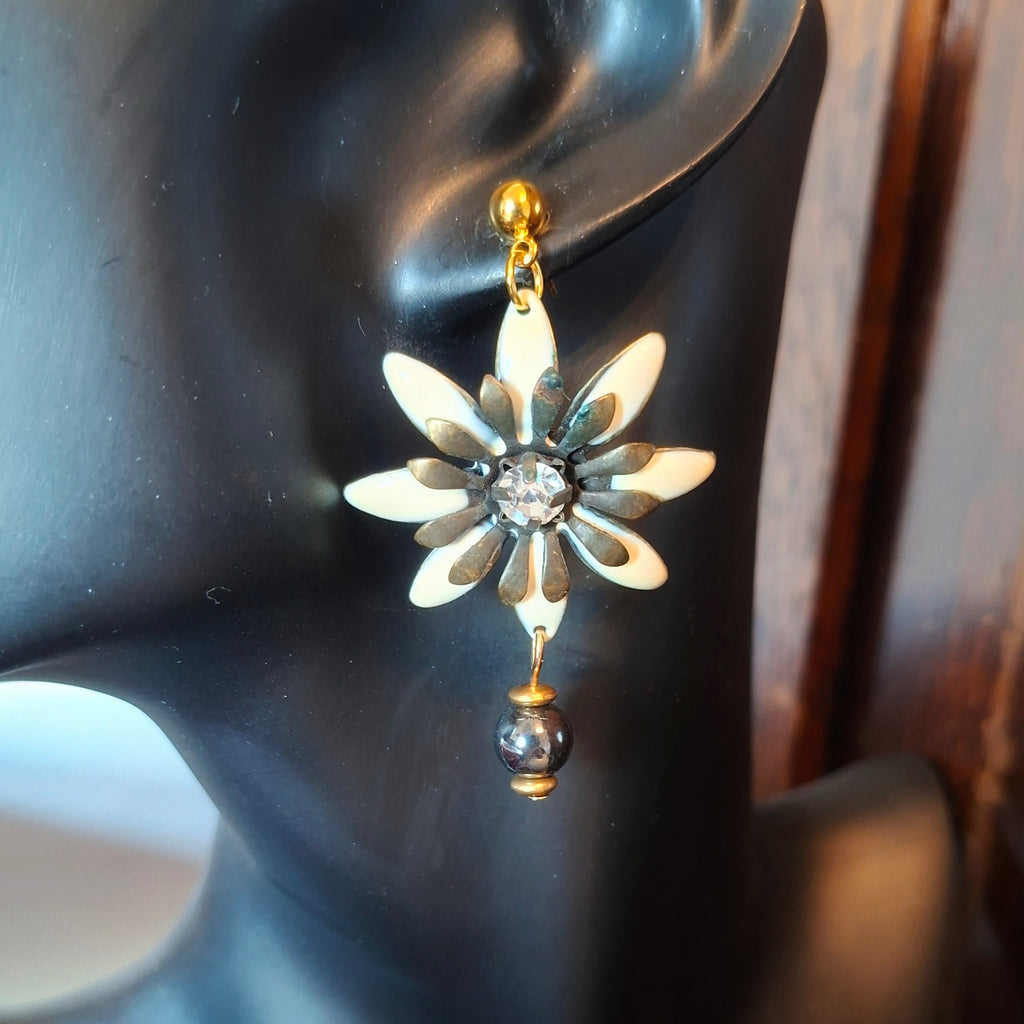 Flower-shaped earring with a central gemstone on a black mannequin ear.