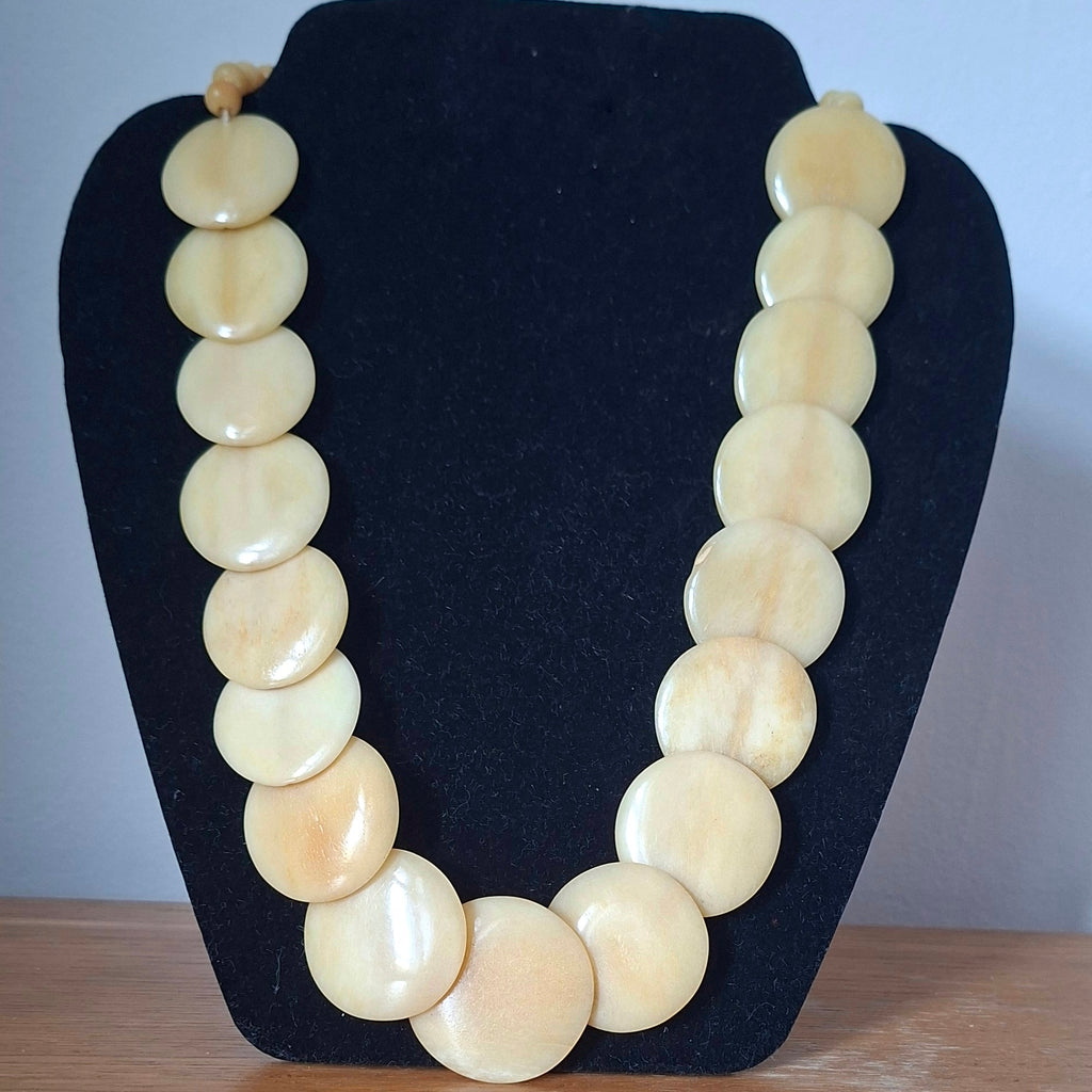 Necklace with large cream-colored beads on a black stand against a light blue background