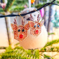 Reindeer-shaped earrings with glittery finish in front of a festive background