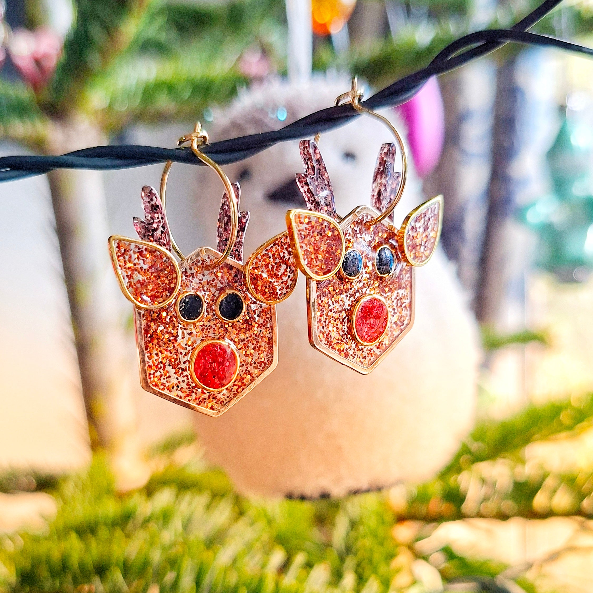 Reindeer-shaped earrings with glittery finish in front of a festive background