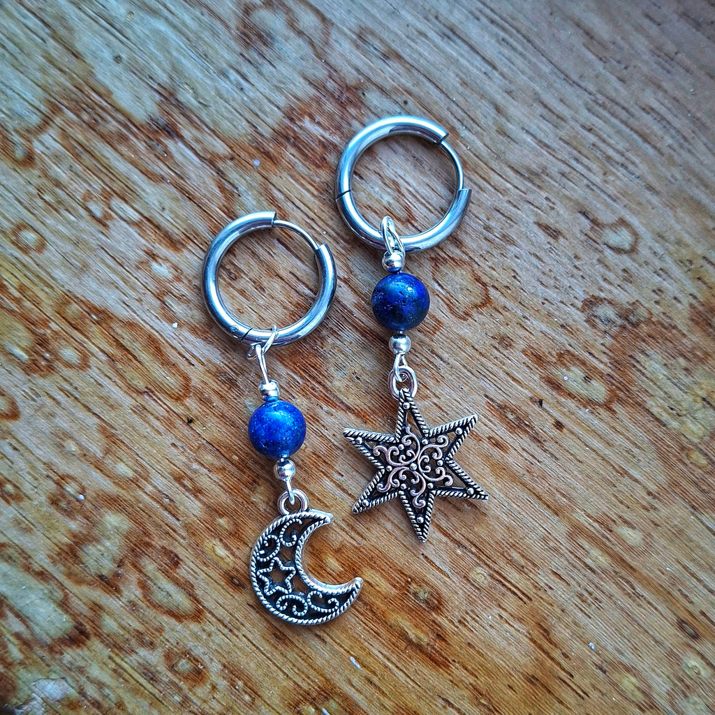Pair of silver hoop earrings with blue beads and star and moon charms on a wooden surface.