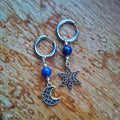 Pair of silver hoop earrings with blue beads and star and moon charms on a wooden surface.