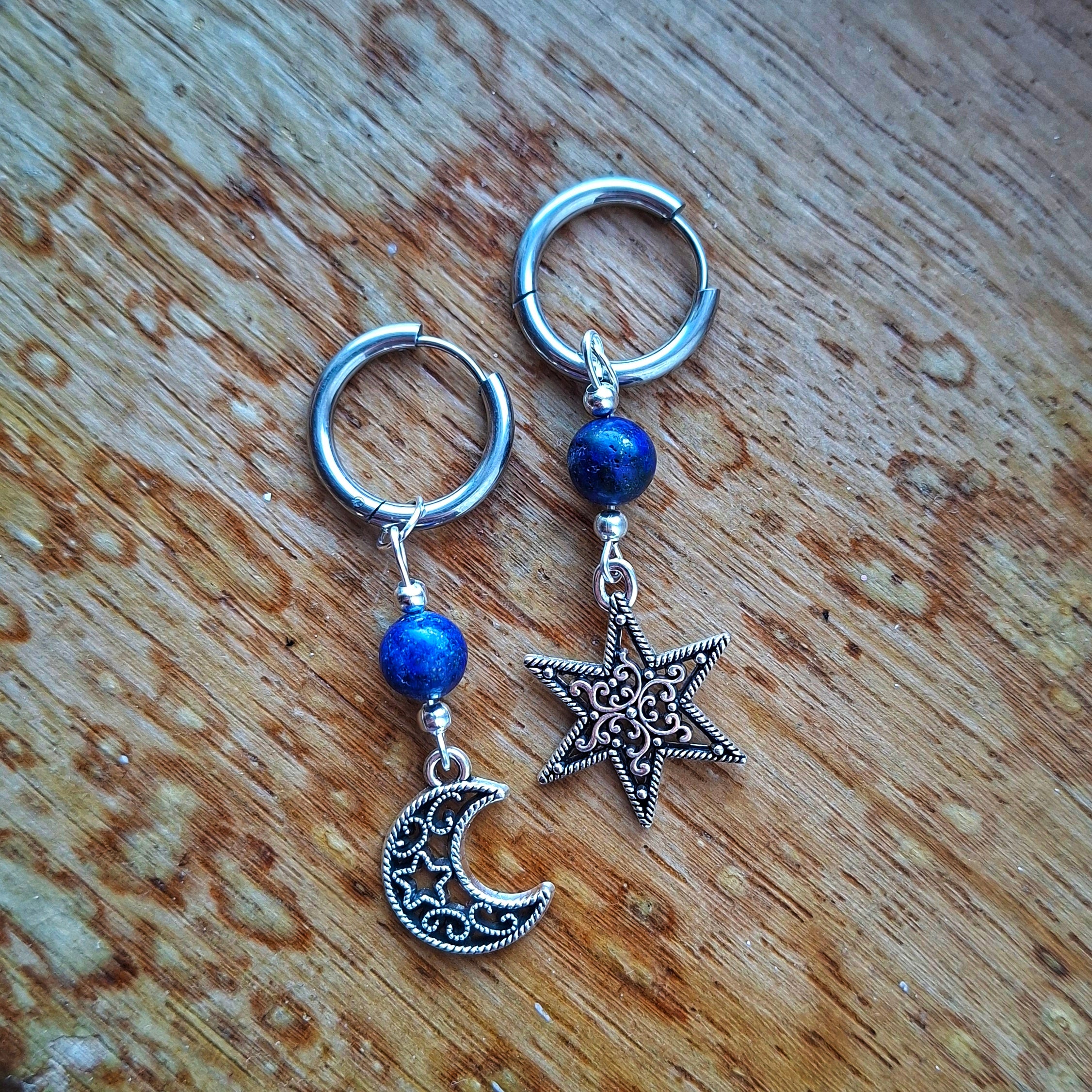Pair of silver hoop earrings with blue beads and star and moon charms on a wooden surface.