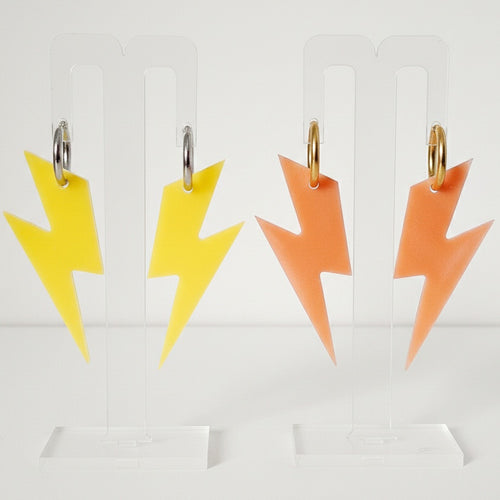 Two pairs of lightning bolt earrings. One is yellow and suspended from titanium steel 15mm hoops. The other are orange and suspended from gold-plated titanium steel 15mm hoops. Made using bio-resin by RainbowRegalia, Greystones, Co. Wicklow.
