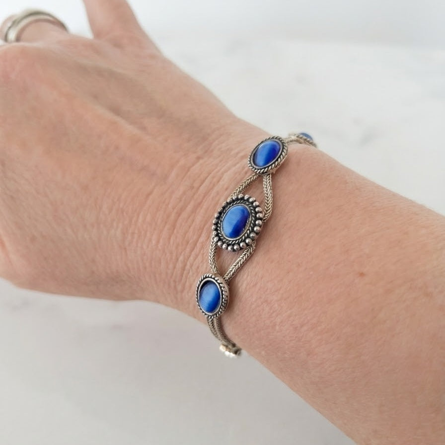 Sterling silver woven chain bracelet with three blue cat’s eye cabochons in decorative rope-edged settings and oxidised filigree accents, on a white background.