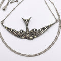 An ornate silver-toned swallow pendant necklace with intricate filigree detailing and small pale yellow gemstone accents, displayed on a clean white background.