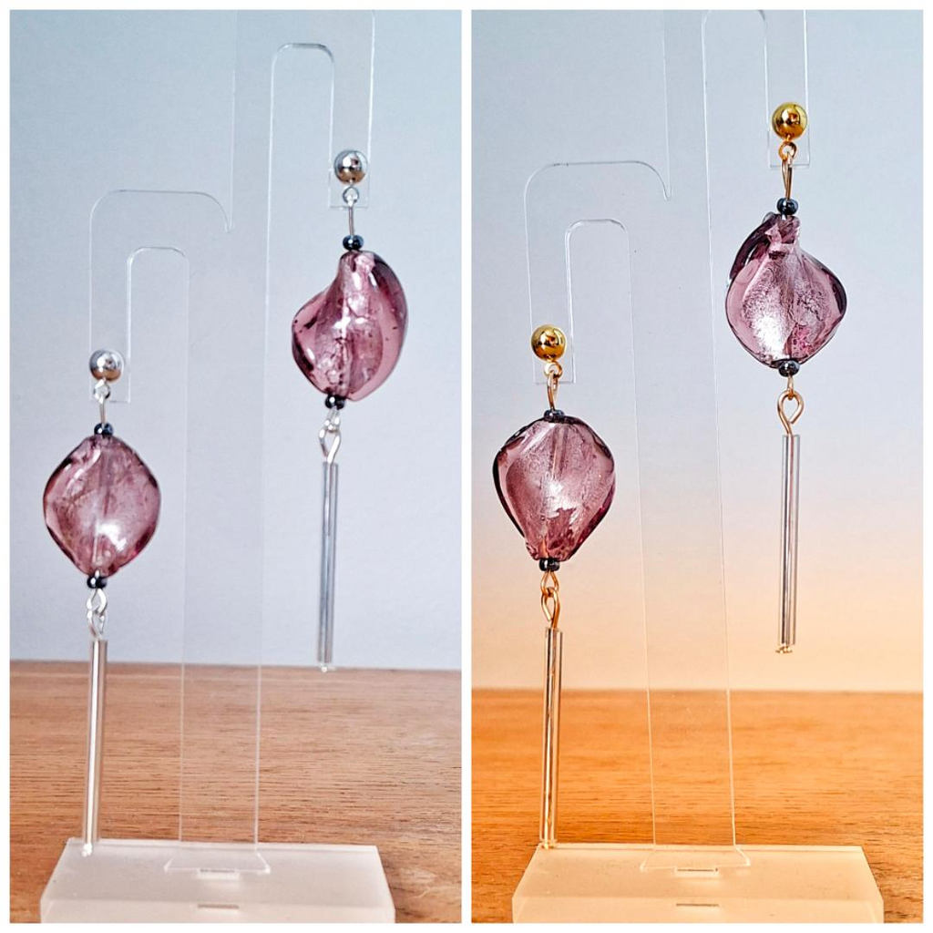 Pair of pink earrings with gold and silver accents on clear stands against a light blue and wooden background.