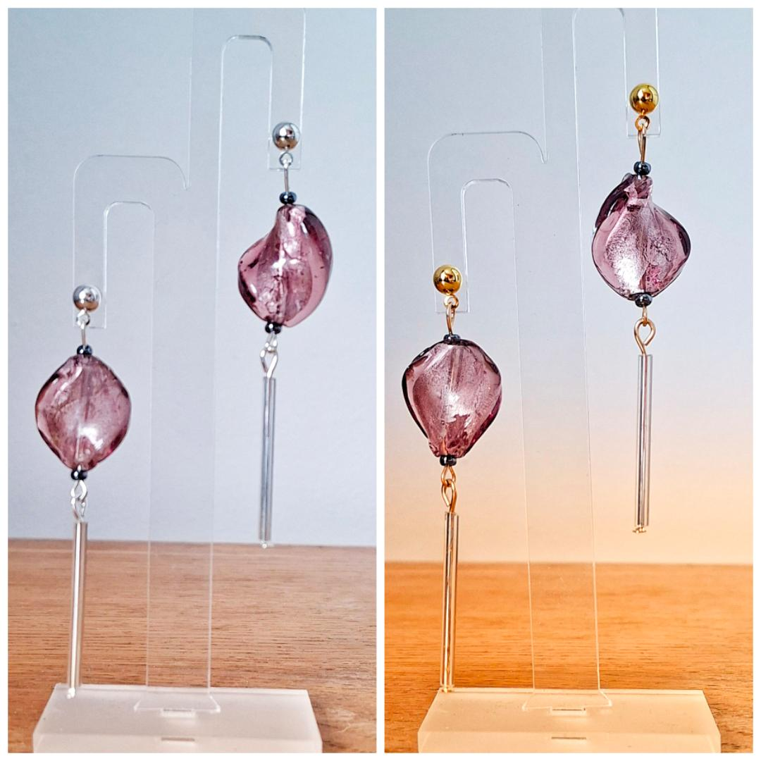 Pair of pink earrings with gold and silver accents on clear stands against a light blue and wooden background.