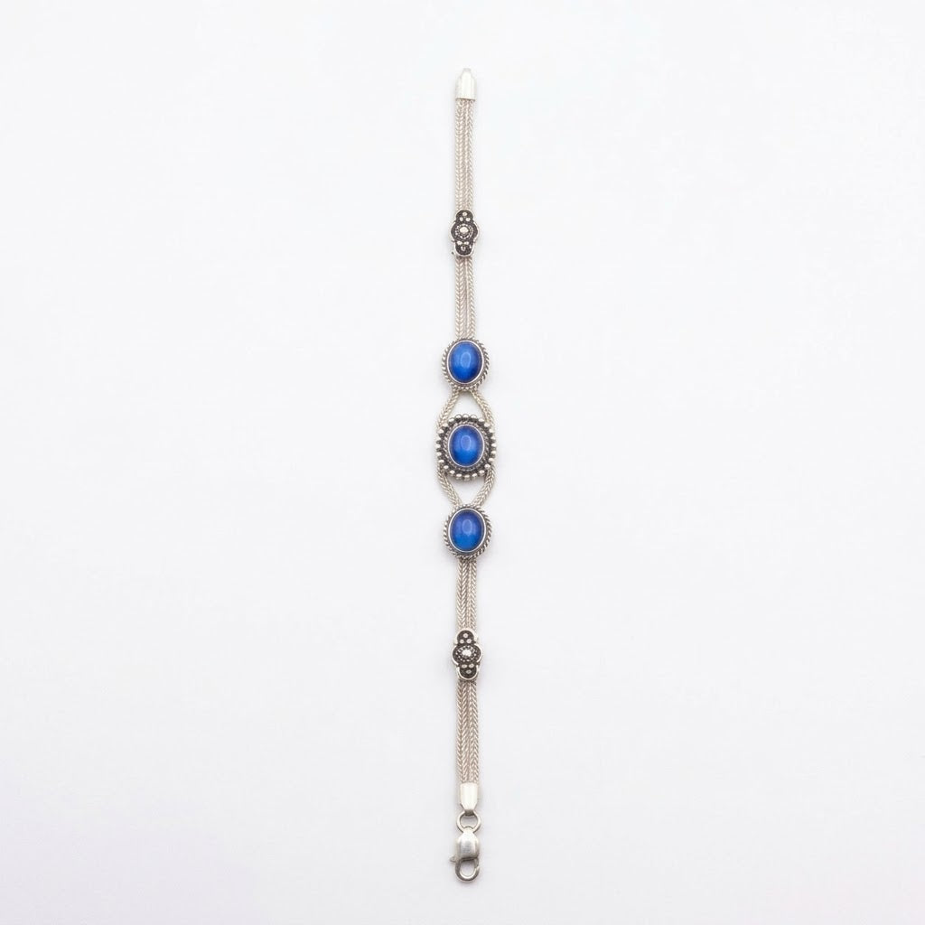Sterling silver woven chain bracelet with three blue cat’s eye cabochons in decorative rope-edged settings and oxidised filigree accents, on a white background.