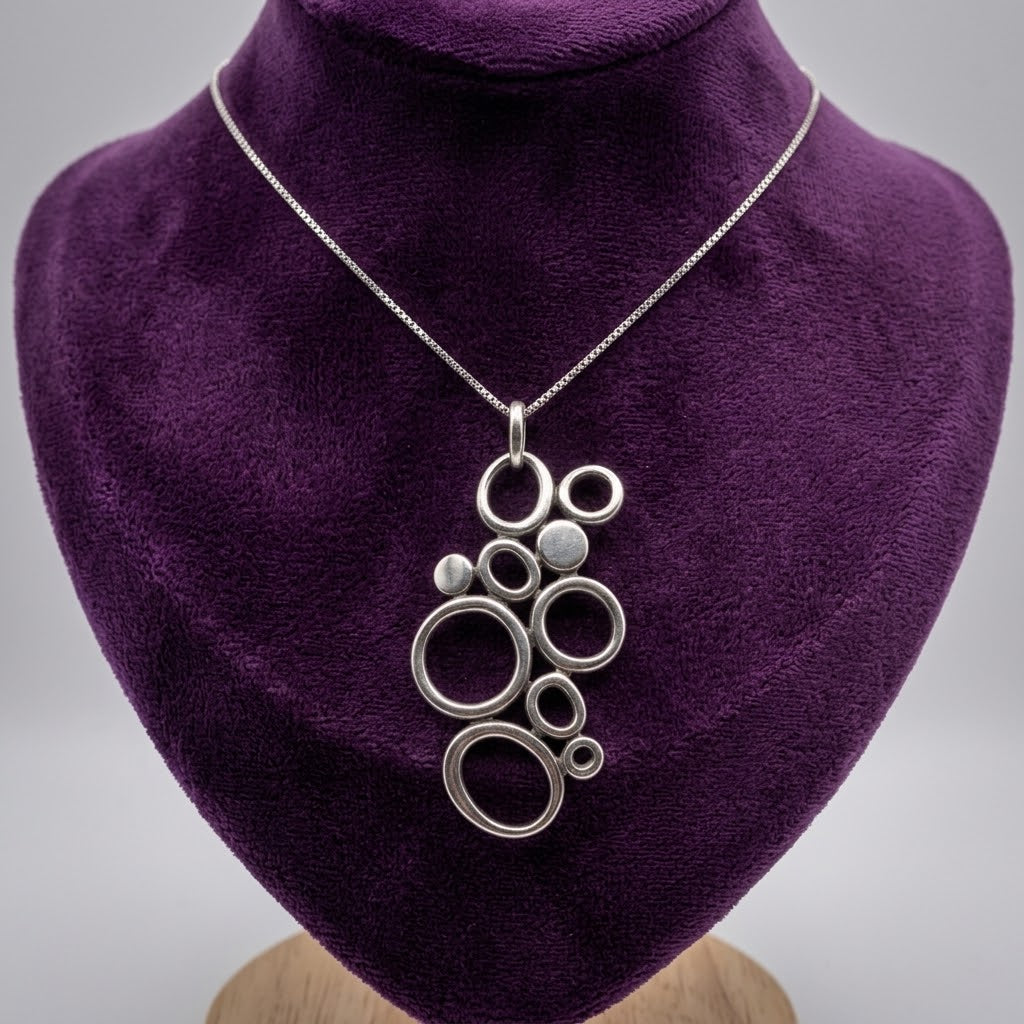 Sterling silver Mexican bubble cluster pendant necklace with interlocking open circles and textured silver discs, displayed on a purple velvet bust.