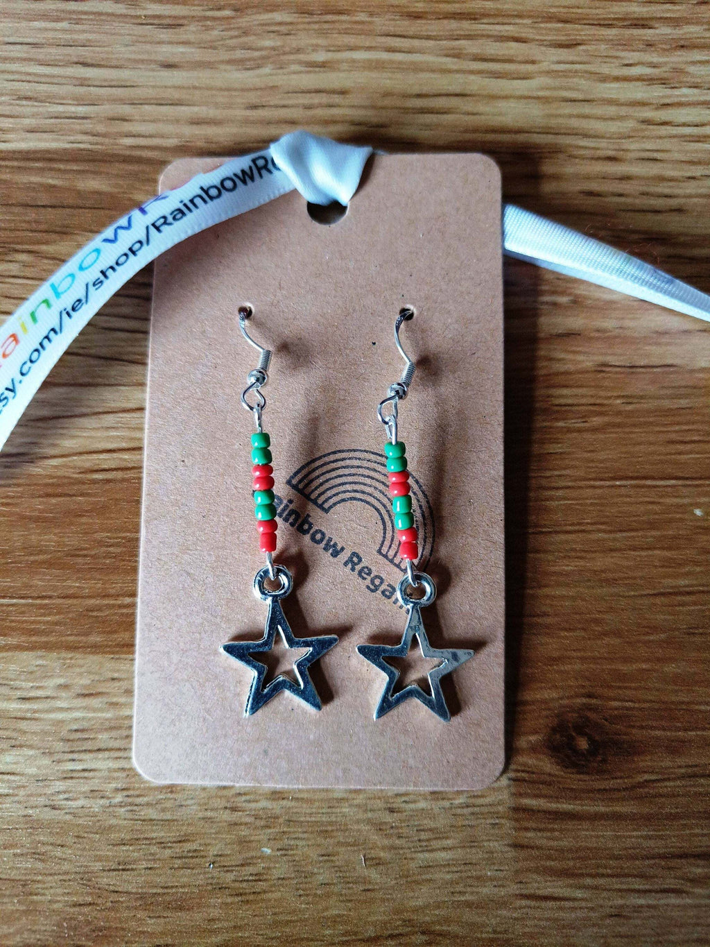 Red and green star earrings with glass seed beads on a rustic display card.