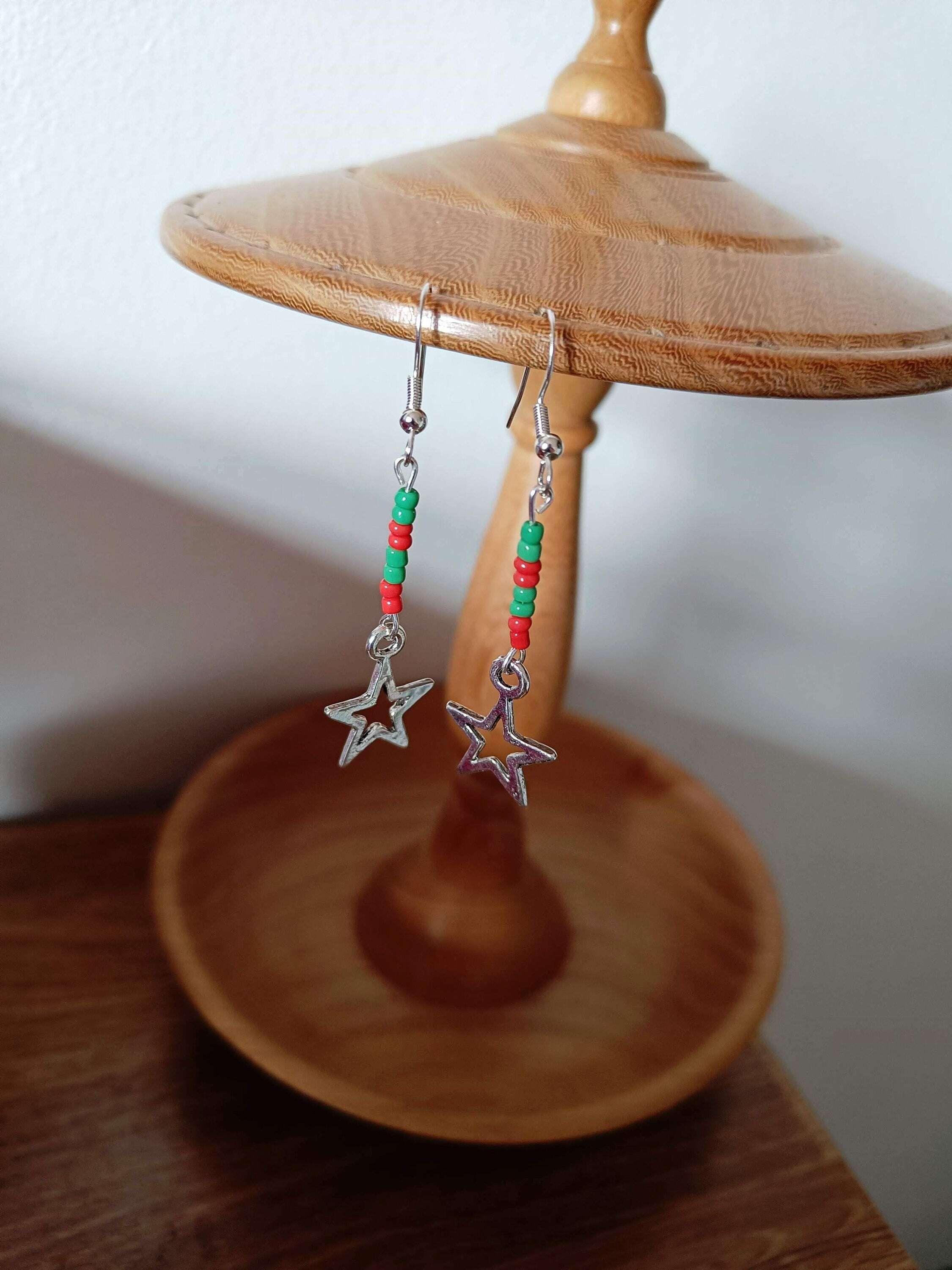 Red and green star earrings made from glass seed beads, hanging on a wooden stand.