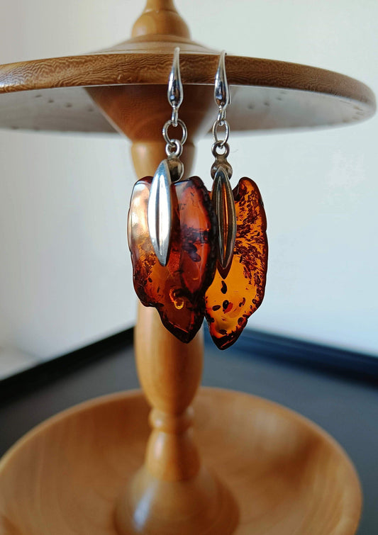 Silver amber earrings with sterling silver ear hooks hanging from a wooden display.