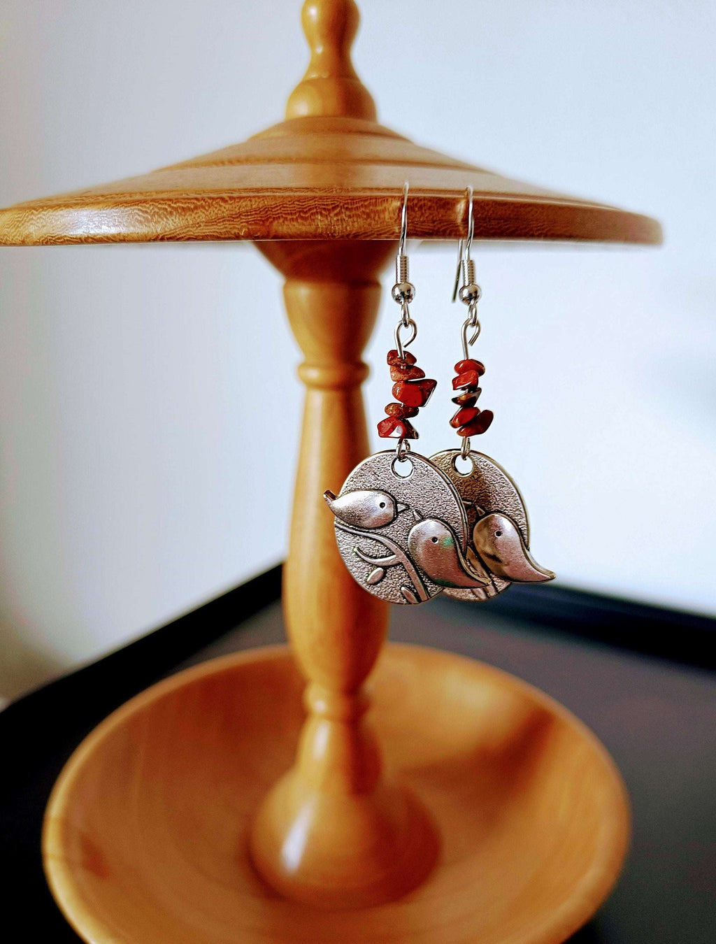 Red Jasper Bird Earrings with silver bird discs hanging on a wooden stand.