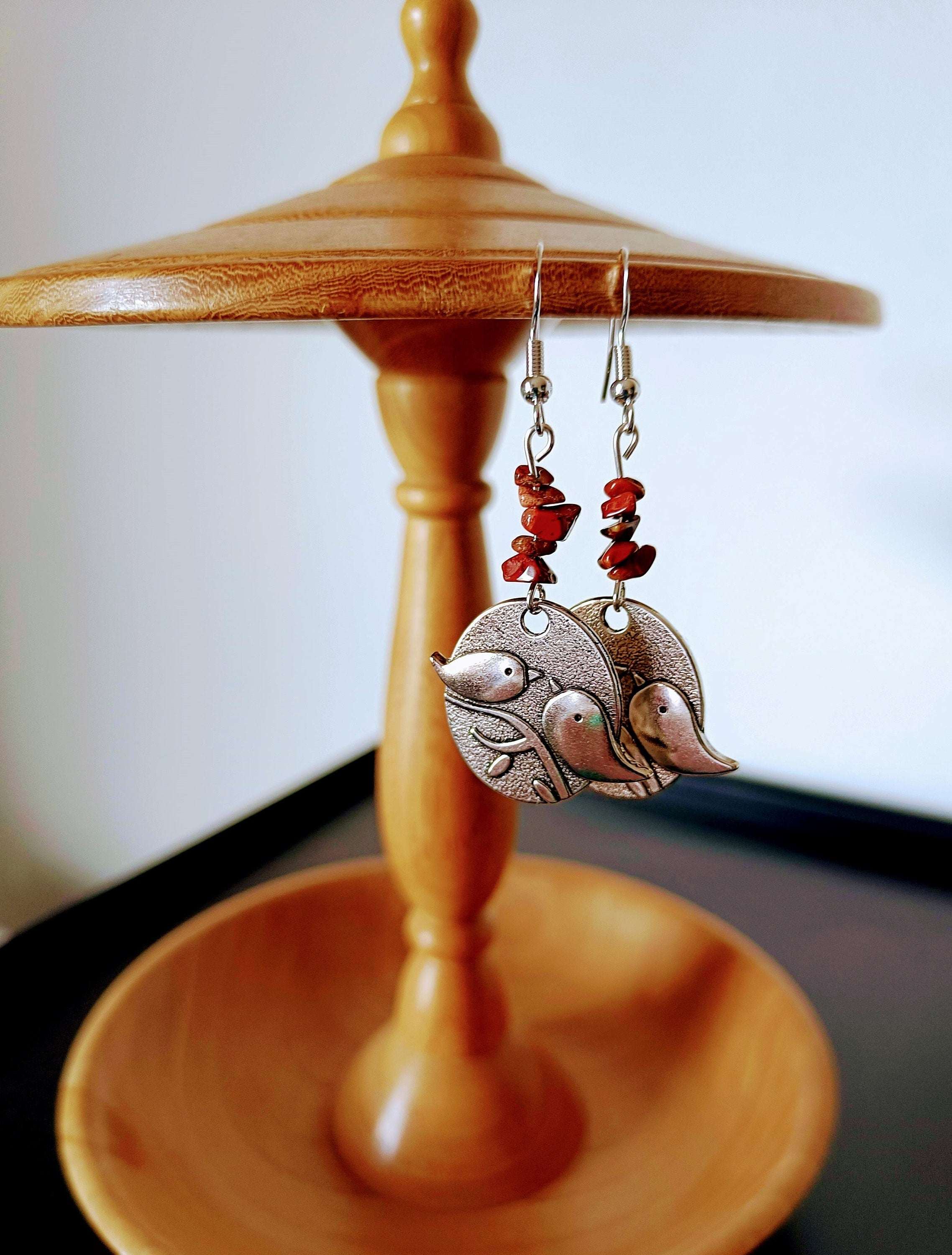 Red Jasper Bird Earrings with silver bird discs hanging on a wooden stand.