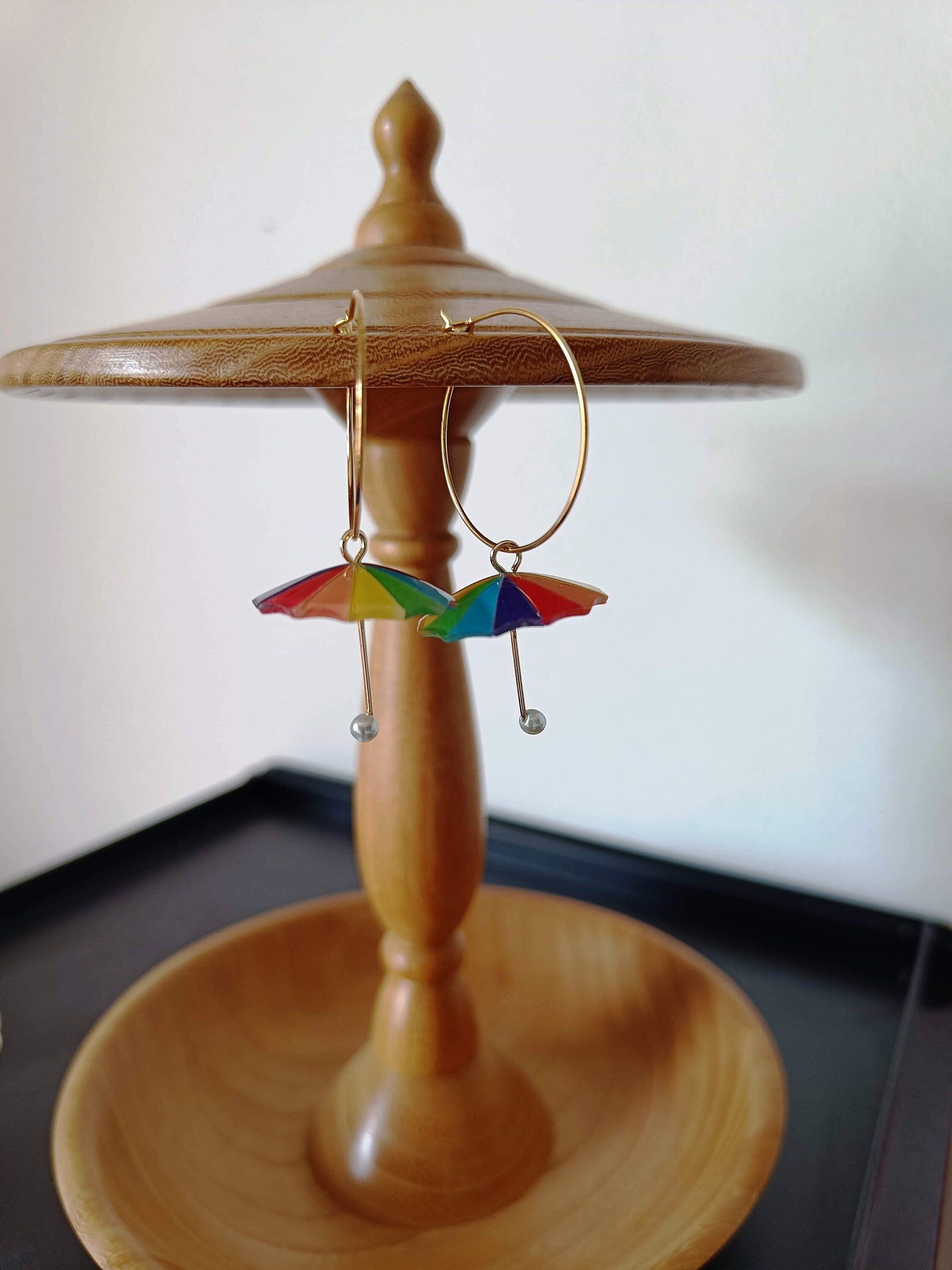 Rainbow umbrella hoop earrings with colorful charms on wooden stand.