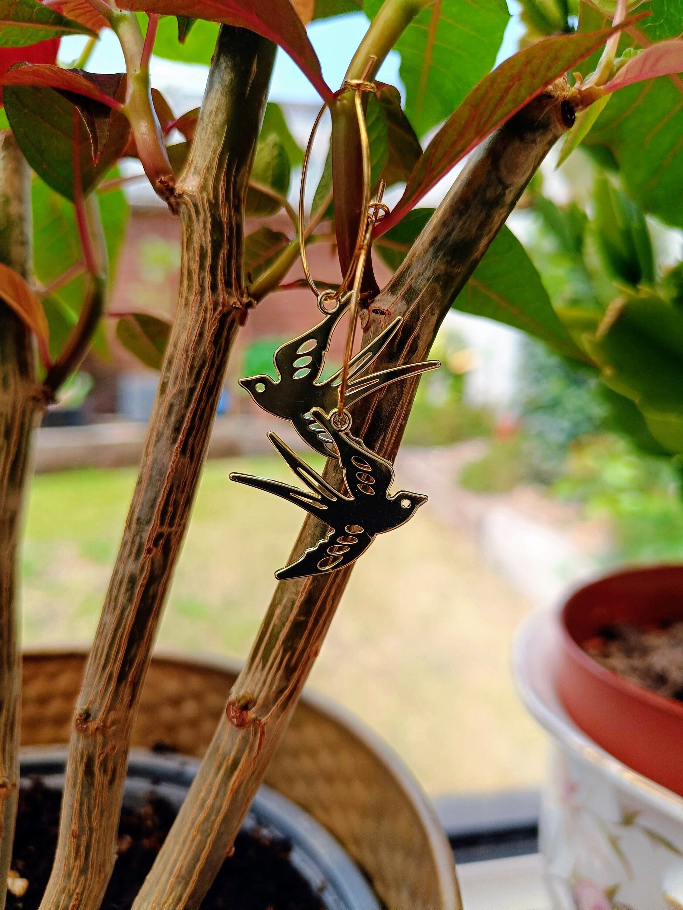 Gold Swallow Hoops featuring swallows in flight, set against a natural background, symbolizing good luck and positivity.