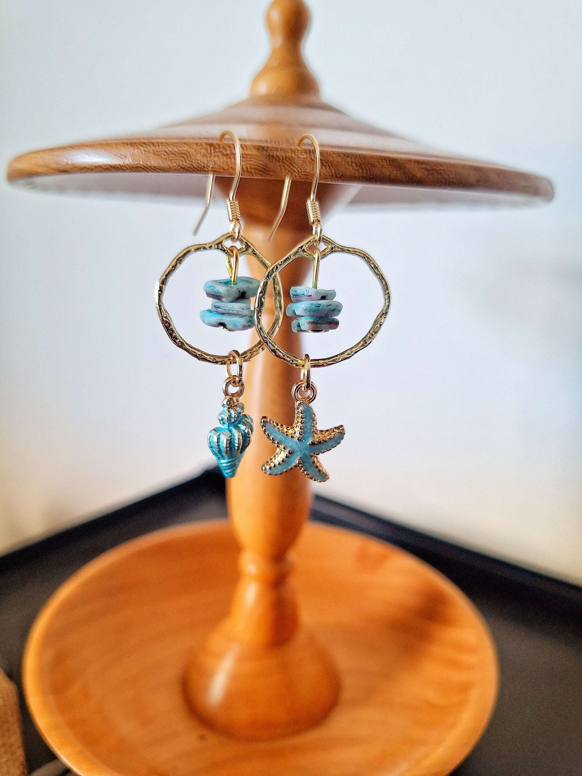 Mismatched shell and starfish earrings with gold detailing on wooden stand.