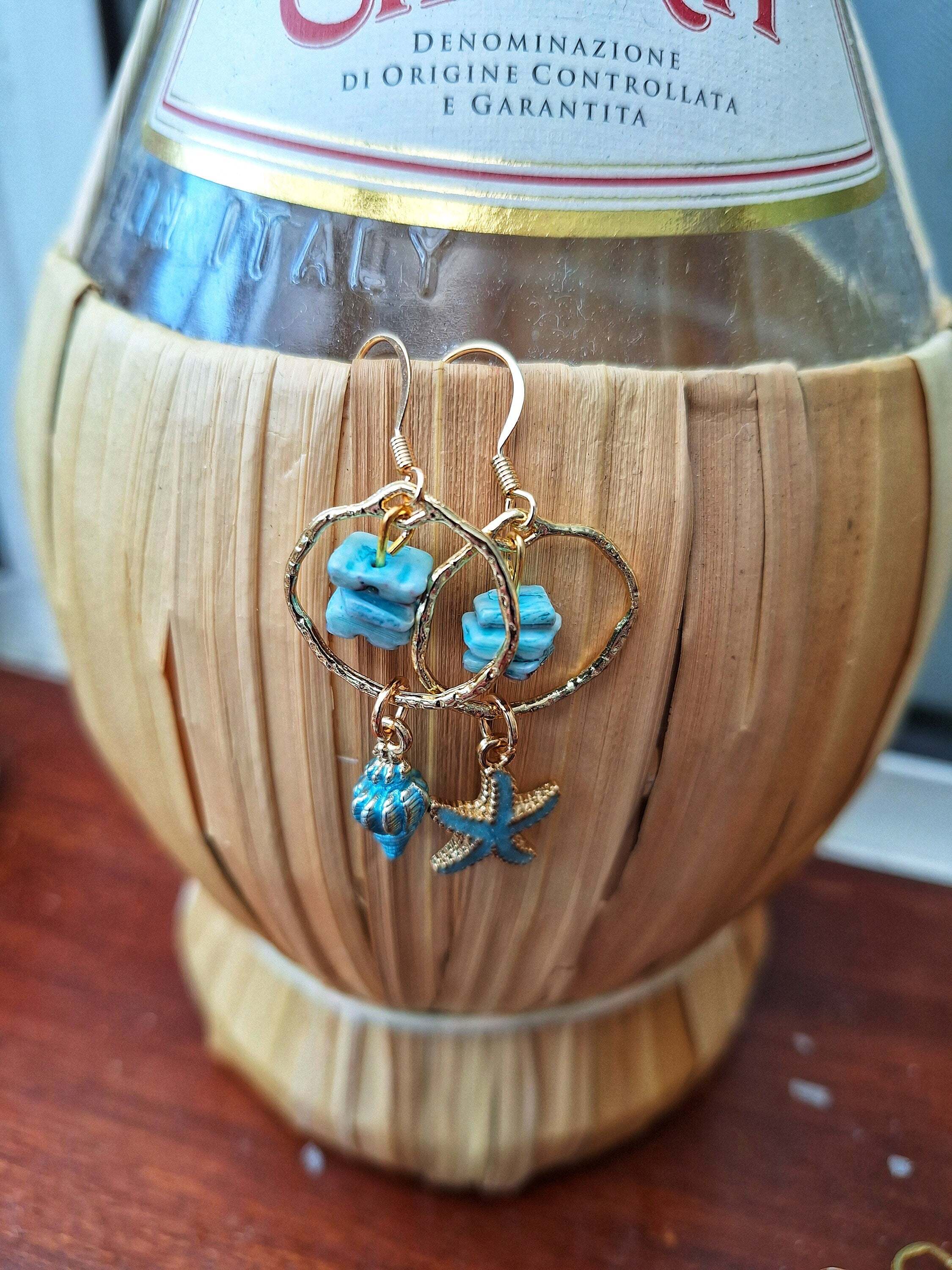 Mismatched shell and starfish earrings with 14K gold ear wires displayed on a wooden background.