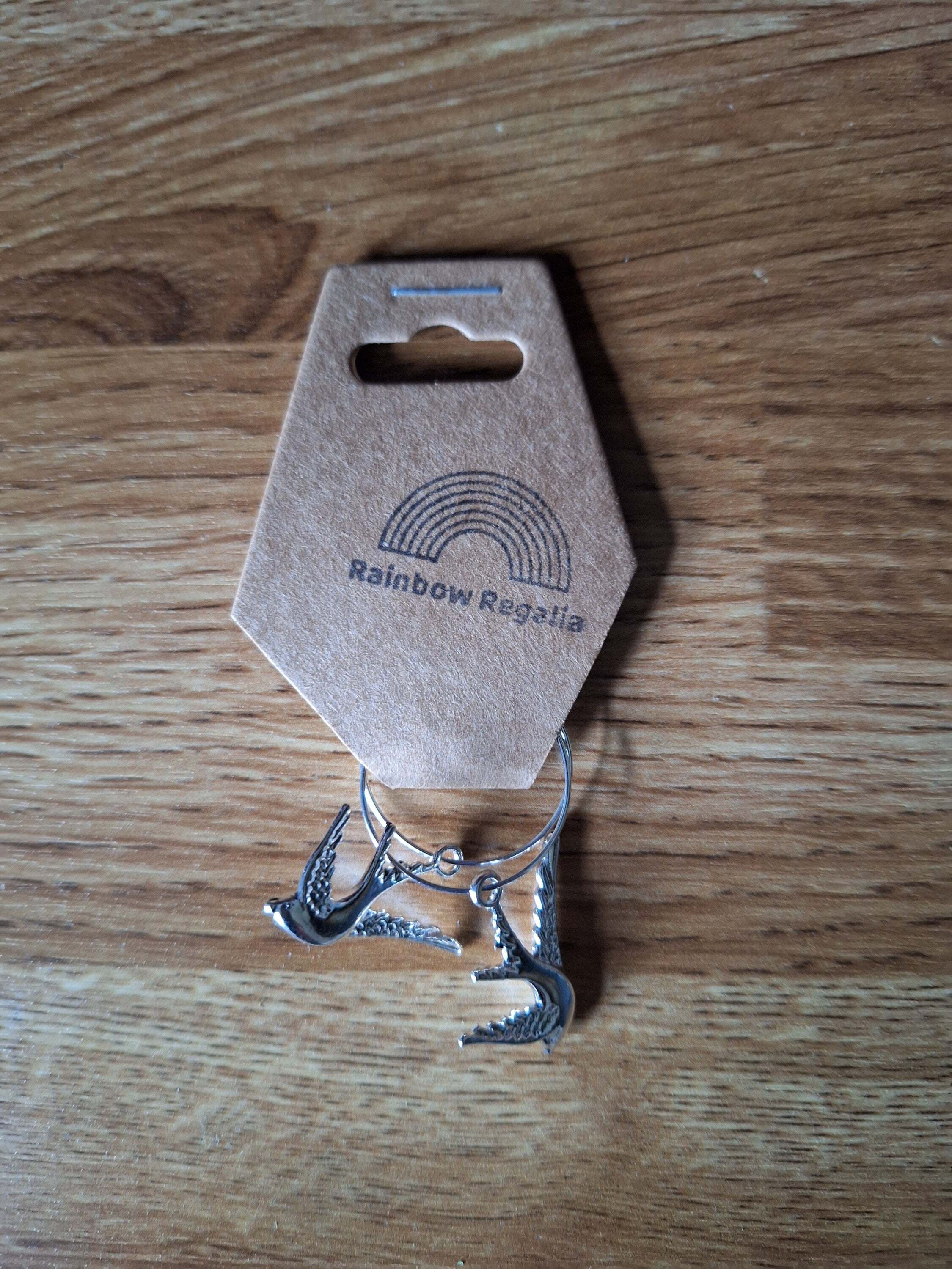 Silver Swallow Hoops with swallow charms on silver-colored brass, elegant accessory on wooden background.