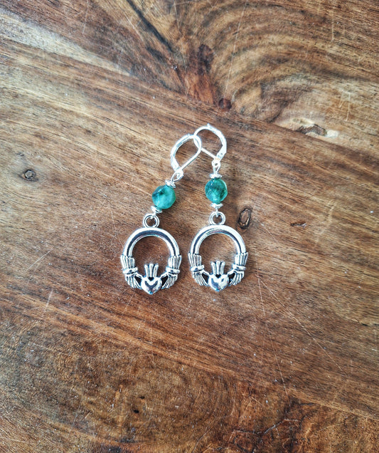 Bébhinn Green Claddagh Earrings with green tourmaline beads and sterling silver Claddagh charms on wooden background.