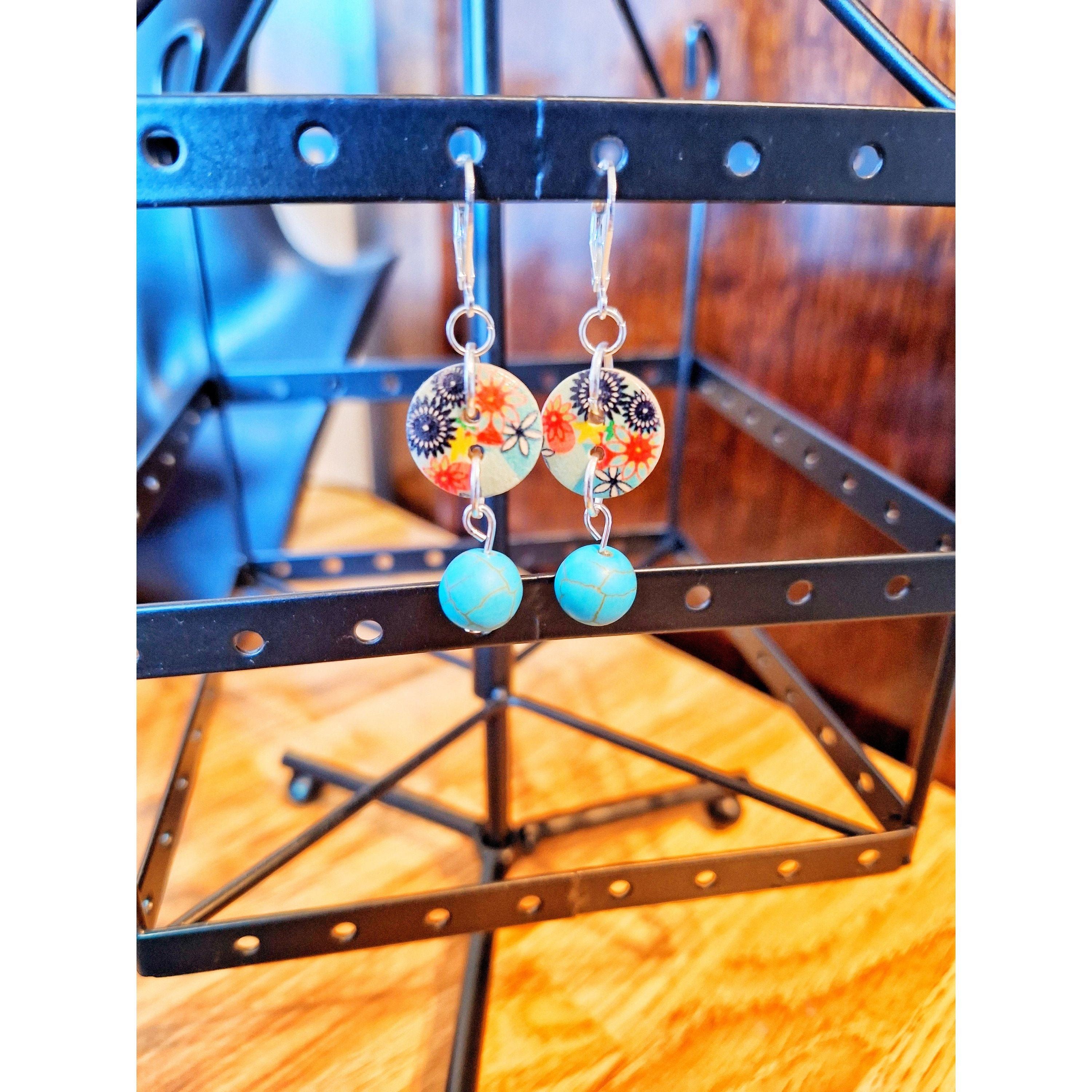 Fleur Drop Earrings with turquoise stones hanging on a black display.