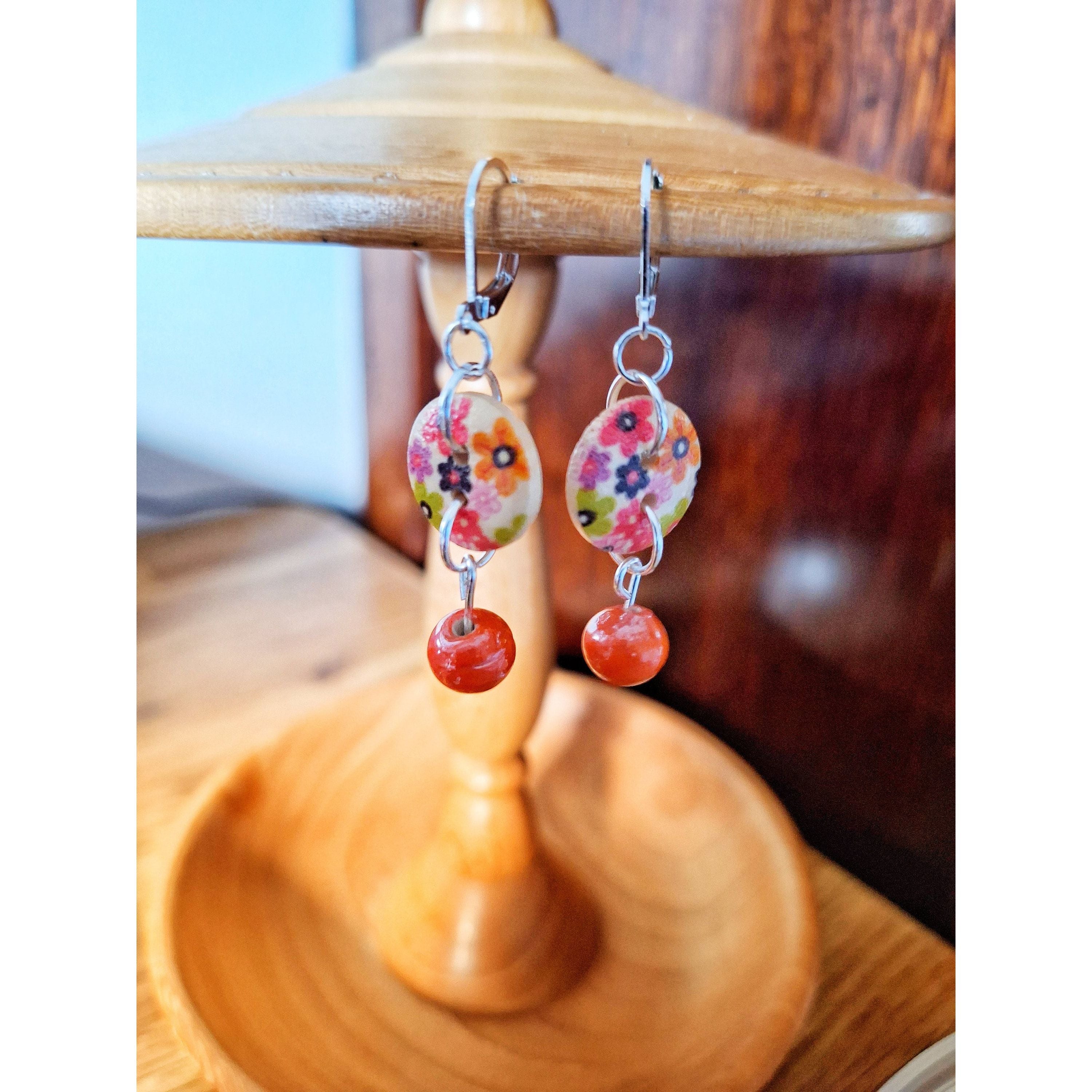 Fleur Drop Earrings with floral design and terracotta beads on wooden background